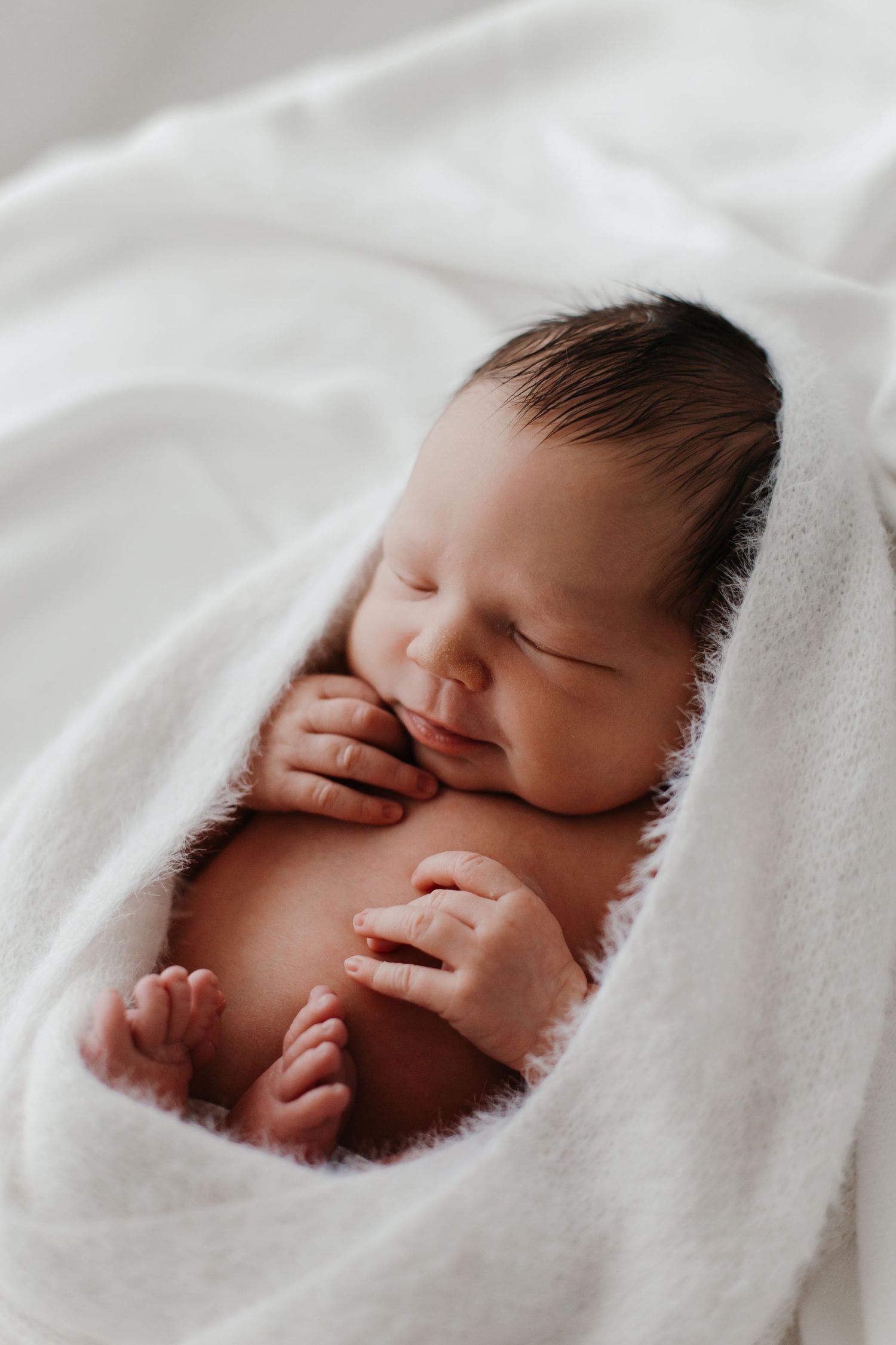 Sleeping newborn wrapped in white blanket during studio session.