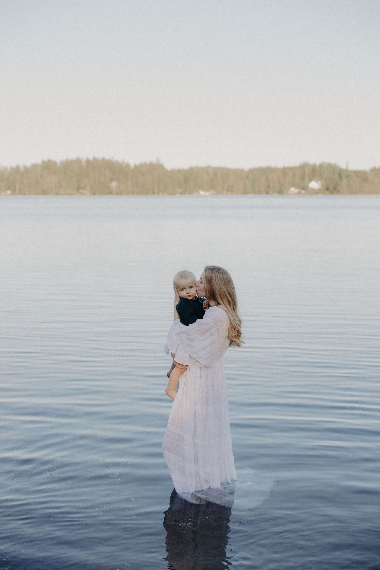 Sweet family moment captured against calm waters and distant treeline.