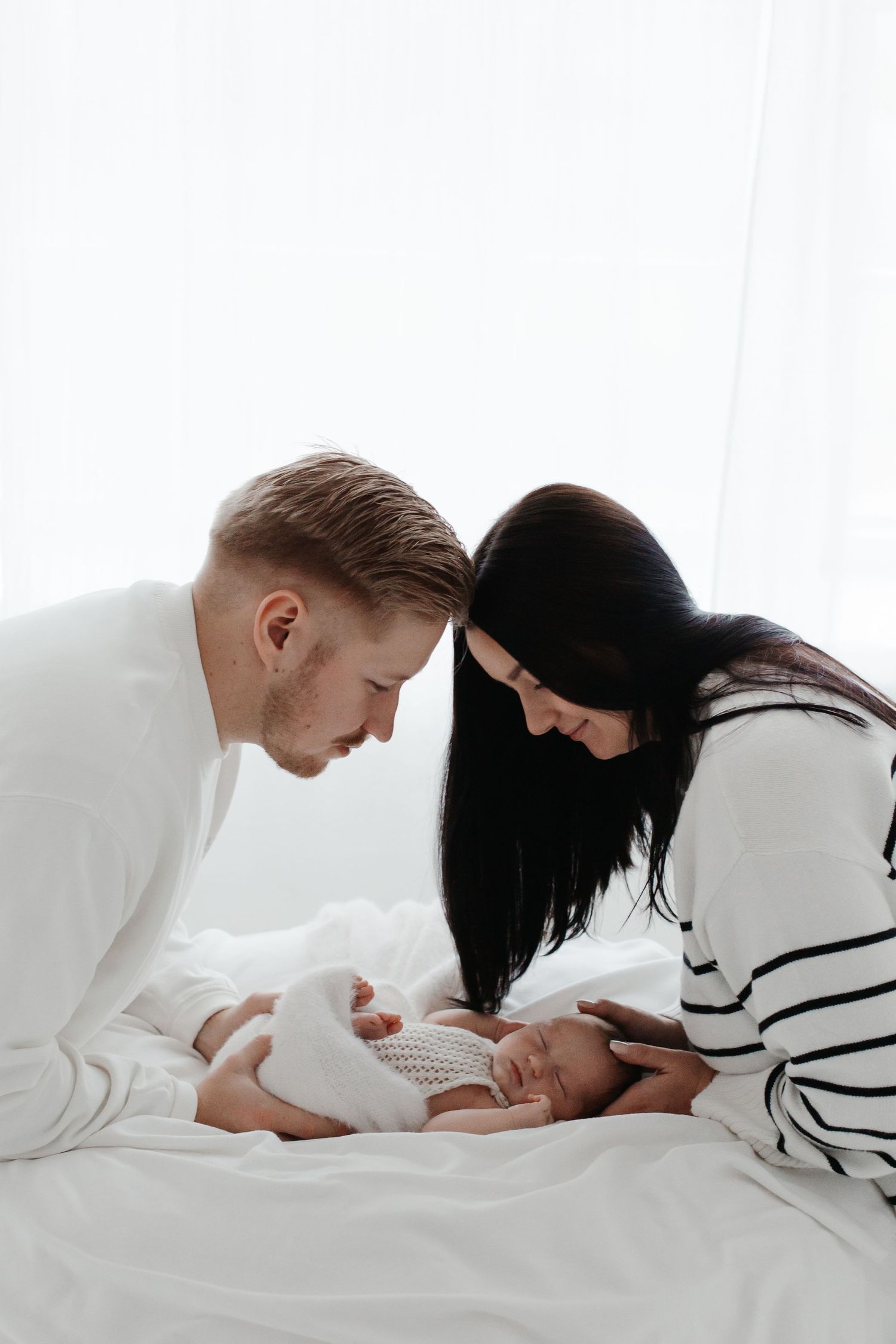 Parents lovingly gazing at their newborn baby on white bedding.