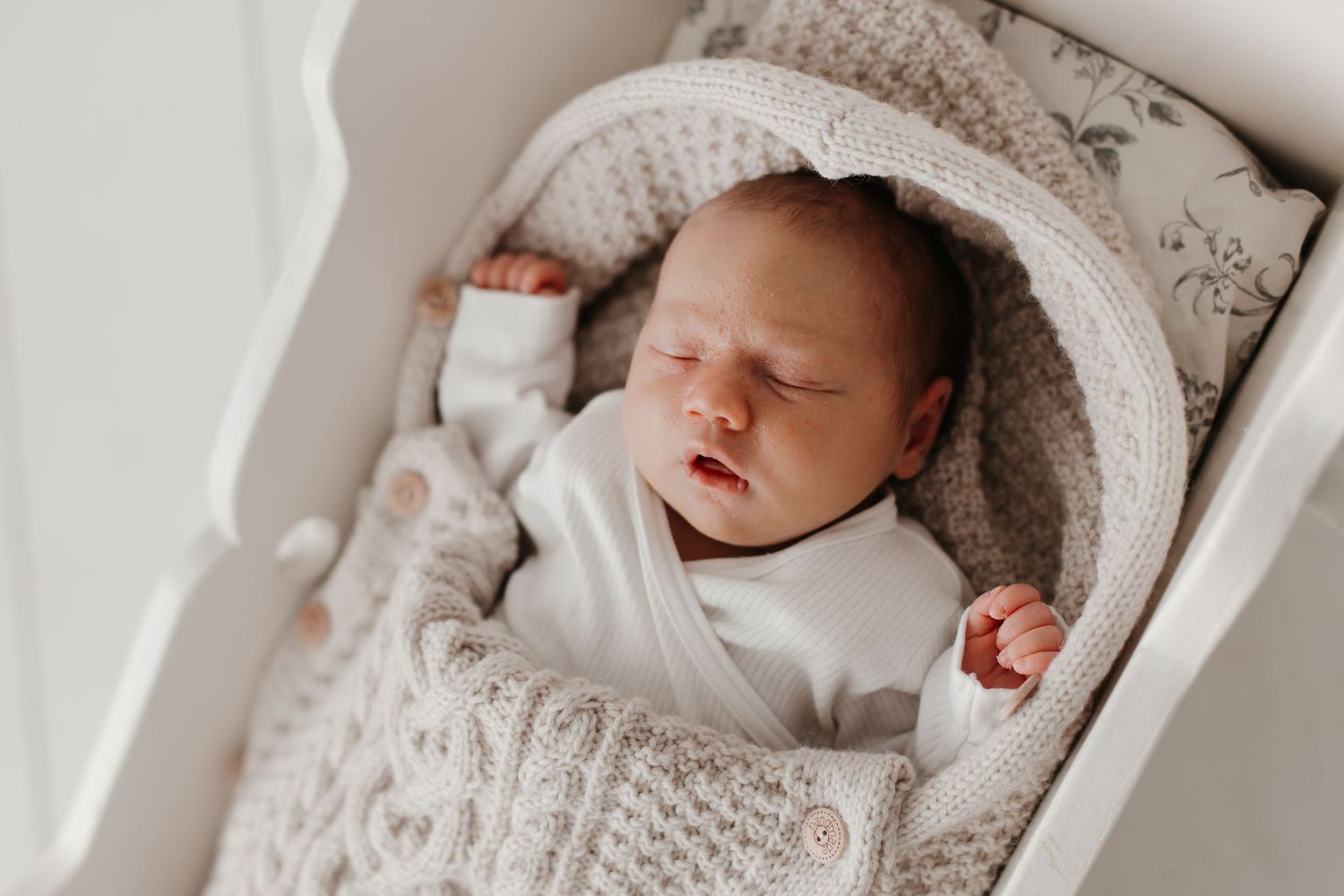 Sleeping newborn baby wrapped in cozy knitted blanket in soft natural light.