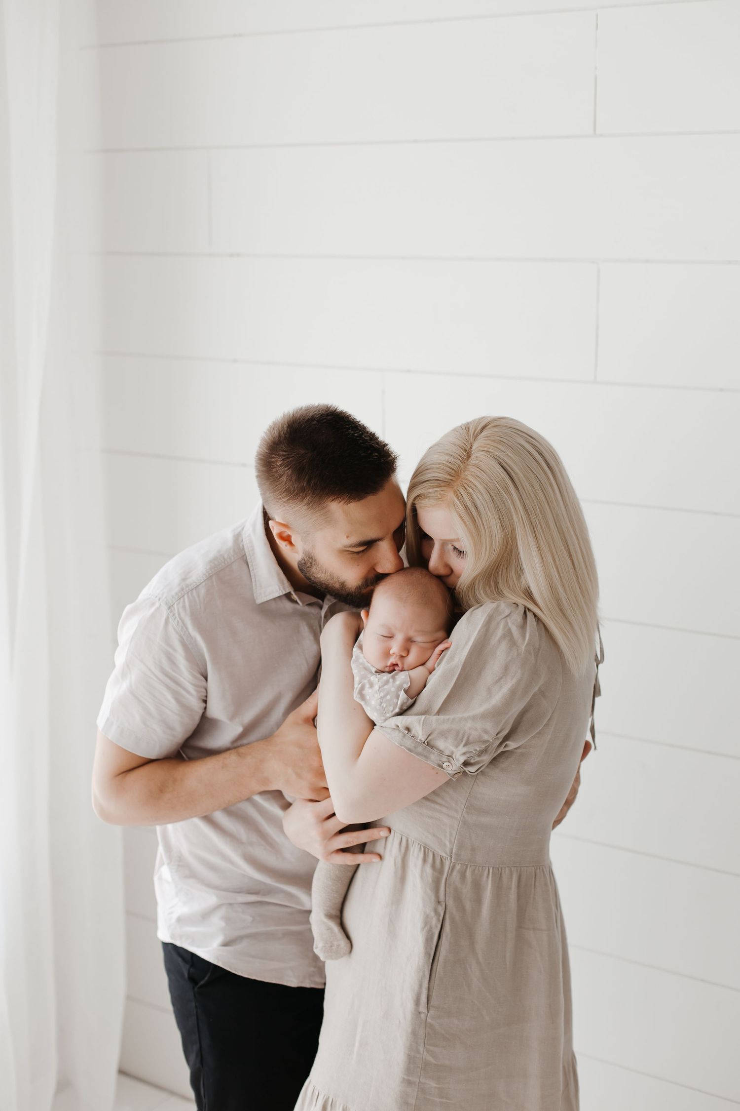 Loving family photo series showing parents taking turns cuddling their small baby in a bright white space.