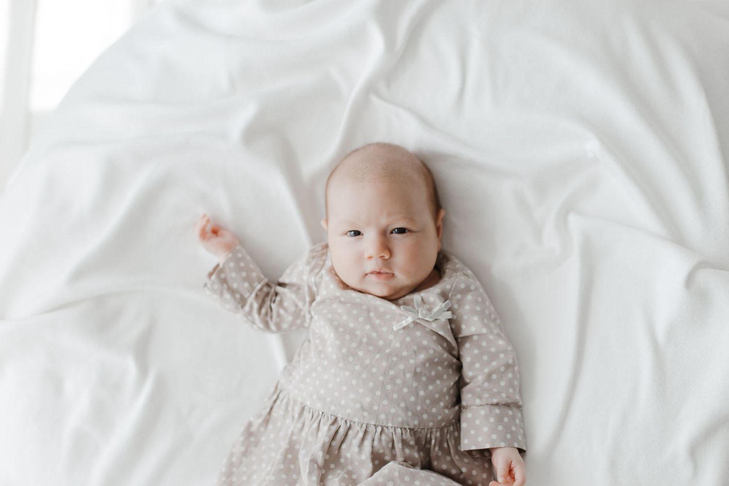 Newborn baby sleeping peacefully on white bedding in natural light.