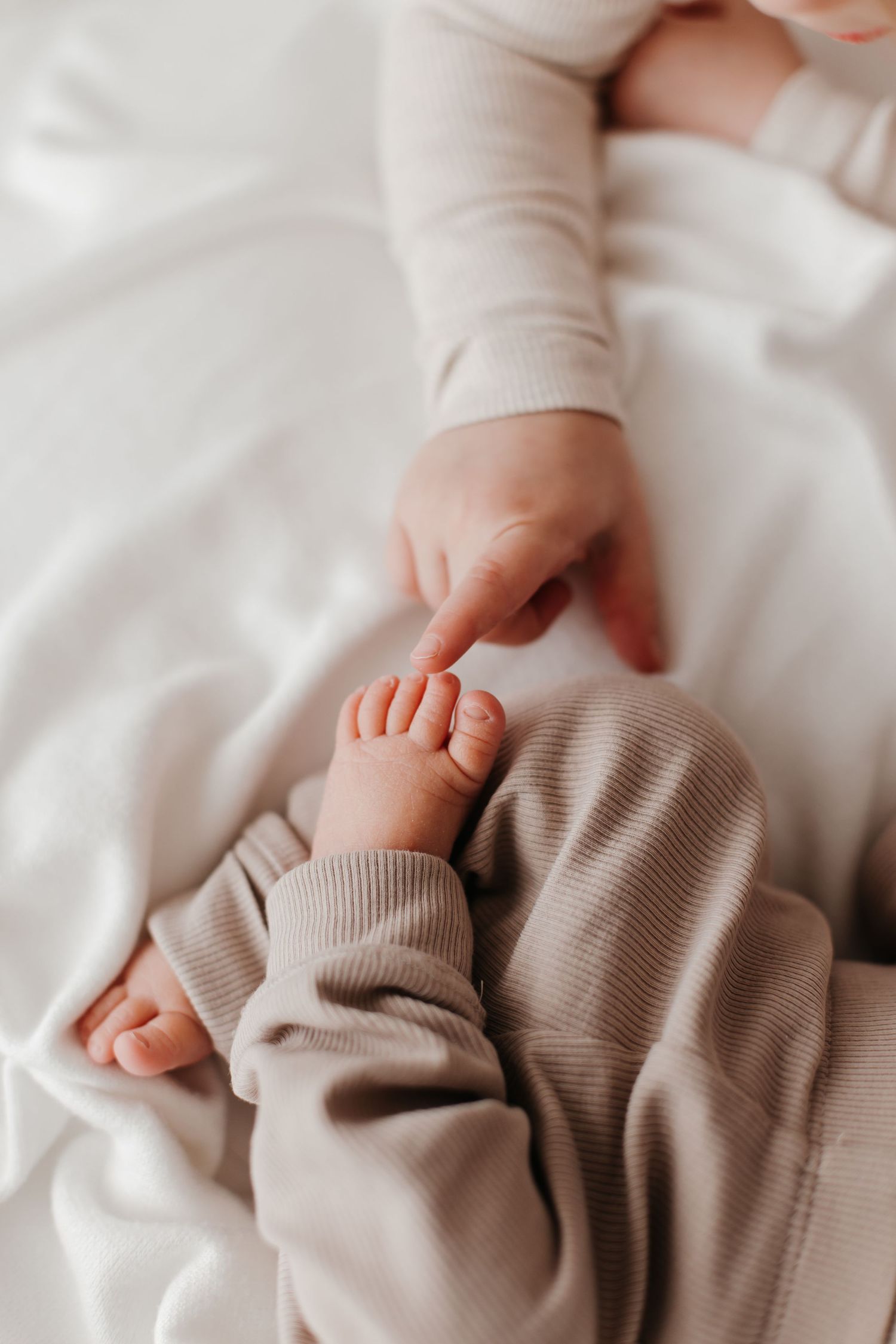 Close-up of tiny baby feet and hands wearing a soft beige sweater against white bedding.