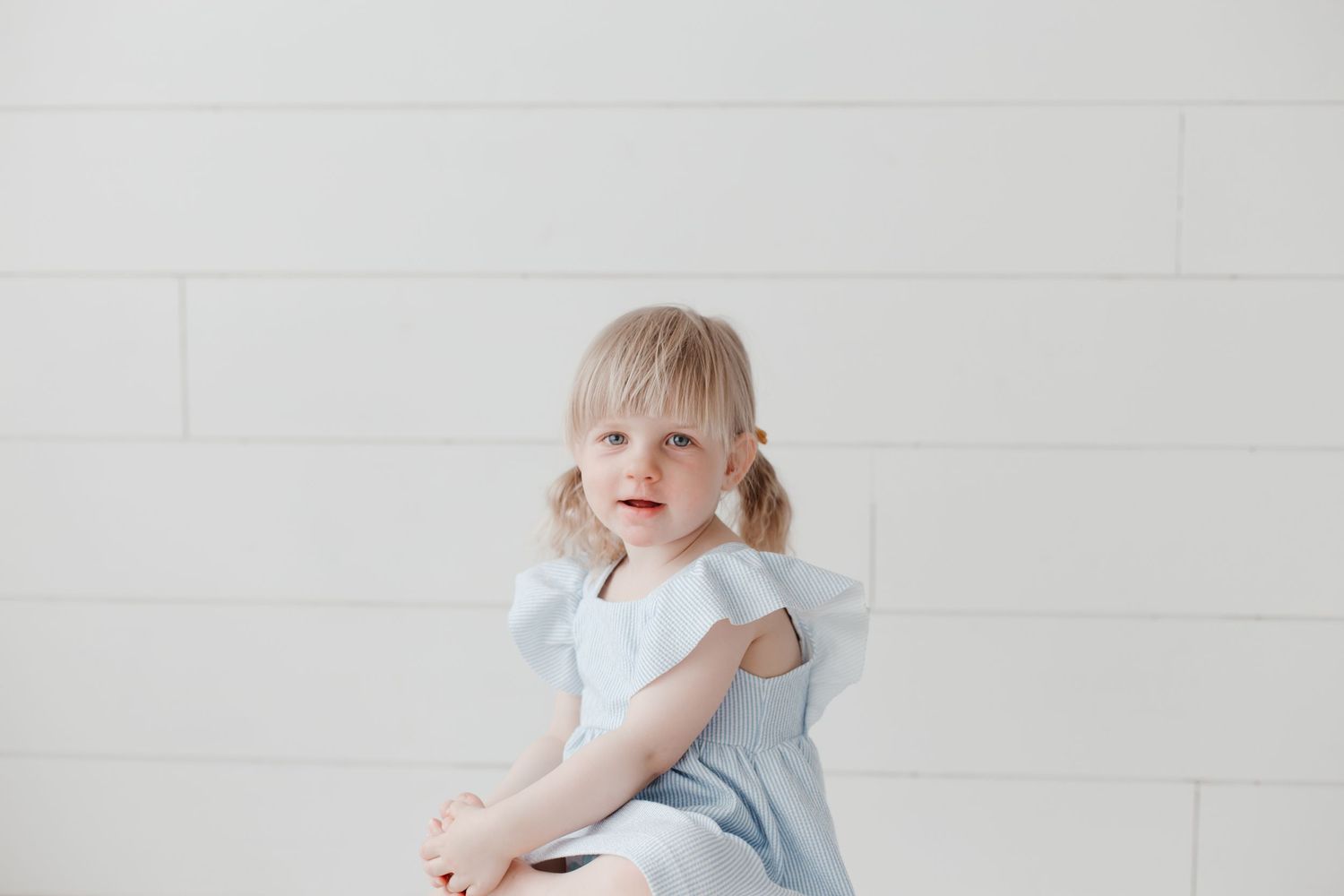 Child in light blue dress playing in bright white room.