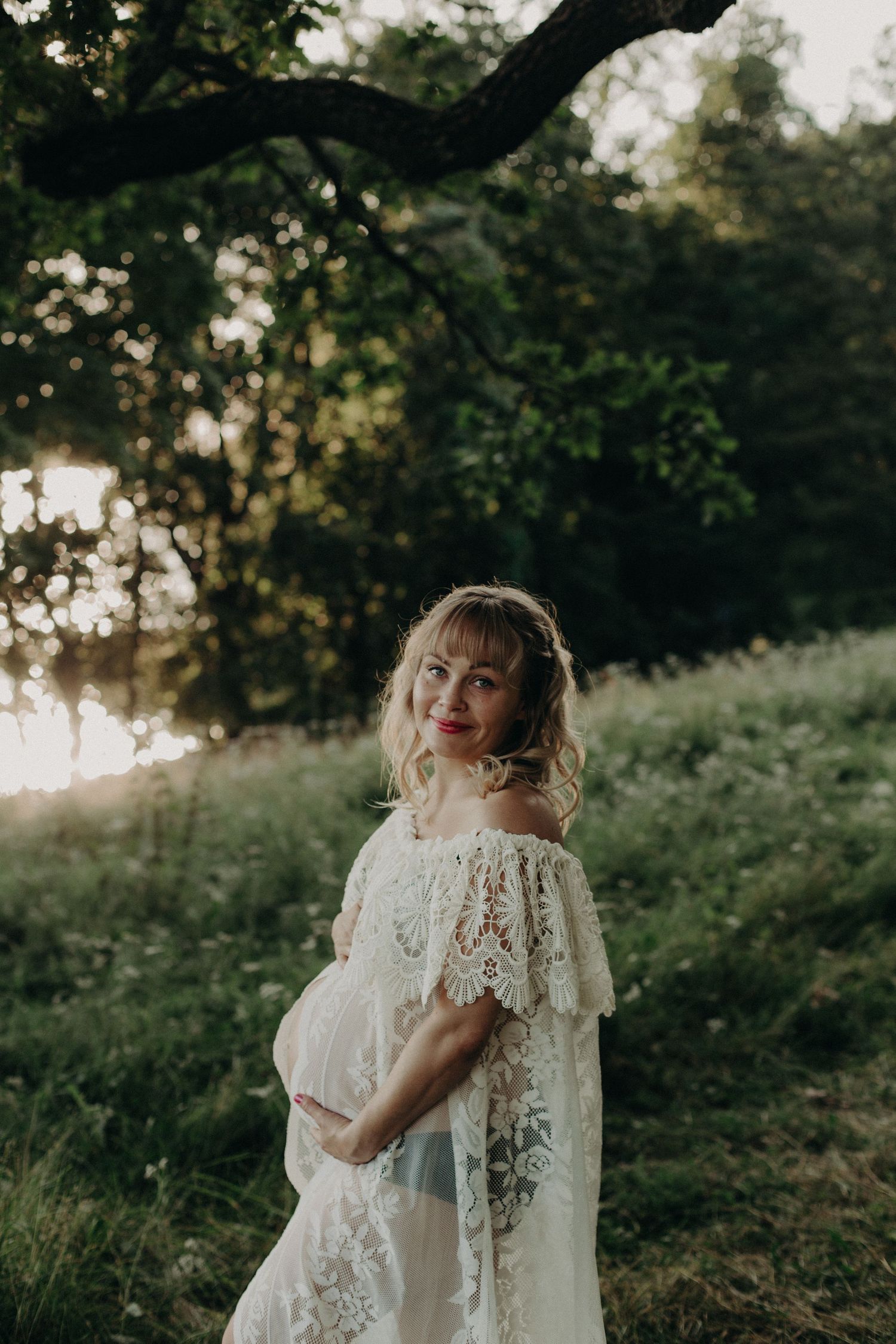 A figure wearing a vintage-style white lace dress poses in a wooded setting.