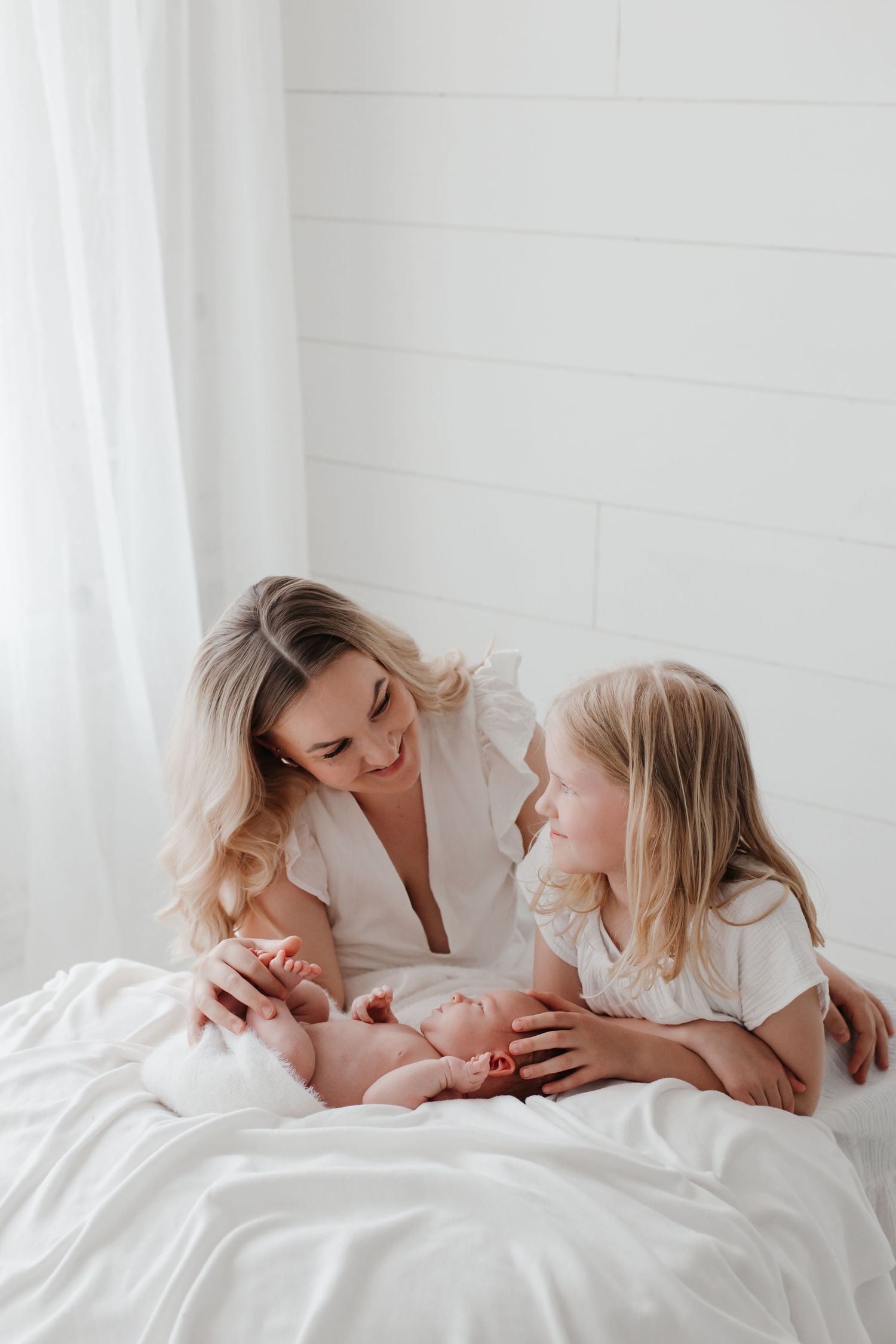 Intimate family moments captured on white bedding in a bright, airy setting.