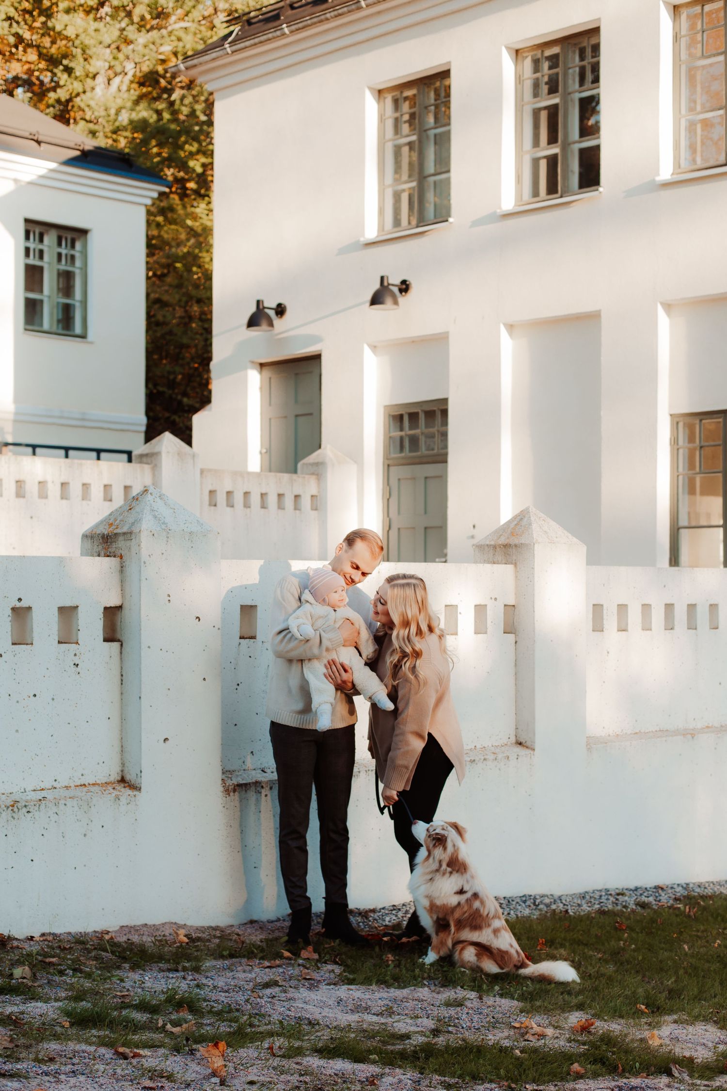 A family shares tender moments against a white building exterior in autumn light.