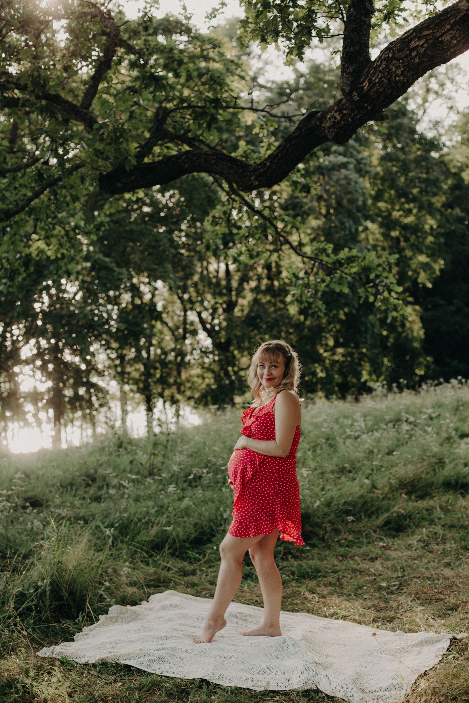 Summer maternity session with red dress against lush green backdrop.