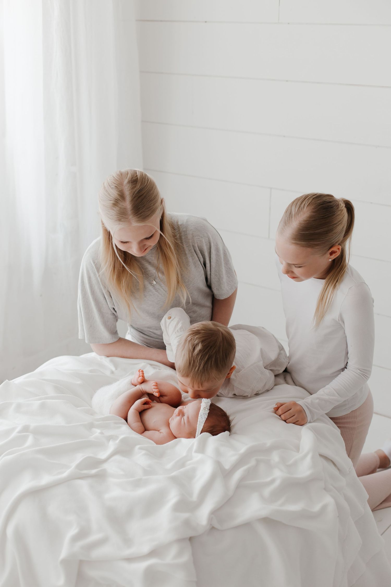 Family gathered on white bed for intimate newborn photo session.