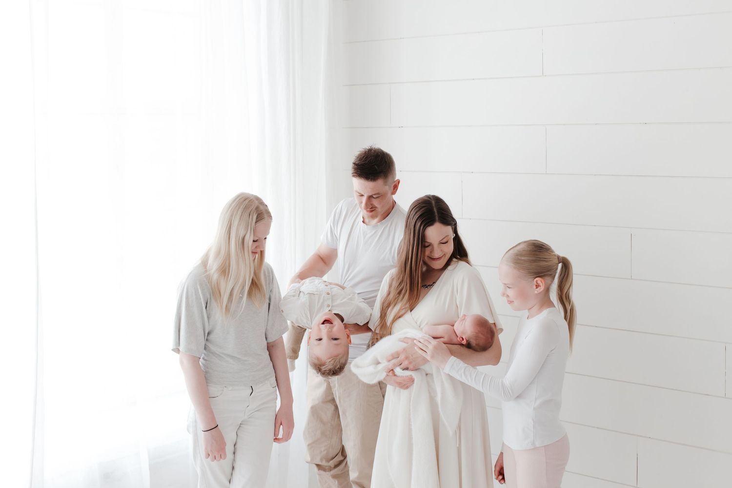 A family in white and neutral tones gathers together in a bright minimalist setting.