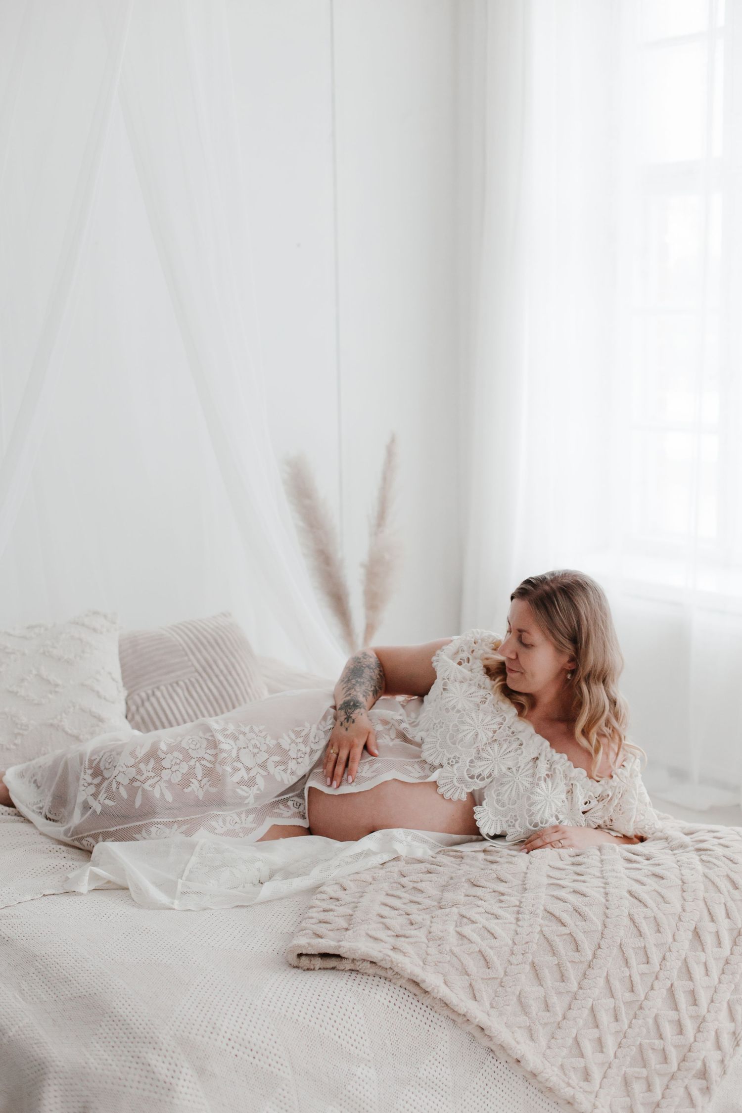 Dreamy maternity boudoir photo with textured bedding and lace details.