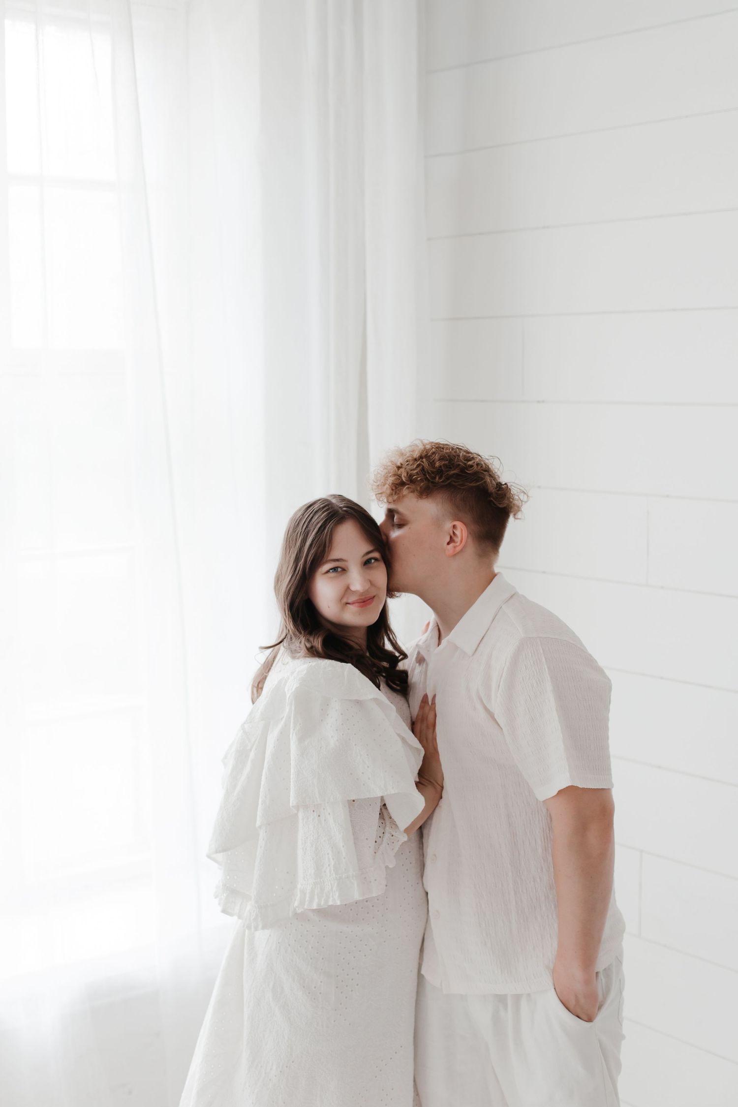 Romantic couple in white shares tender moment in bright minimalist setting.