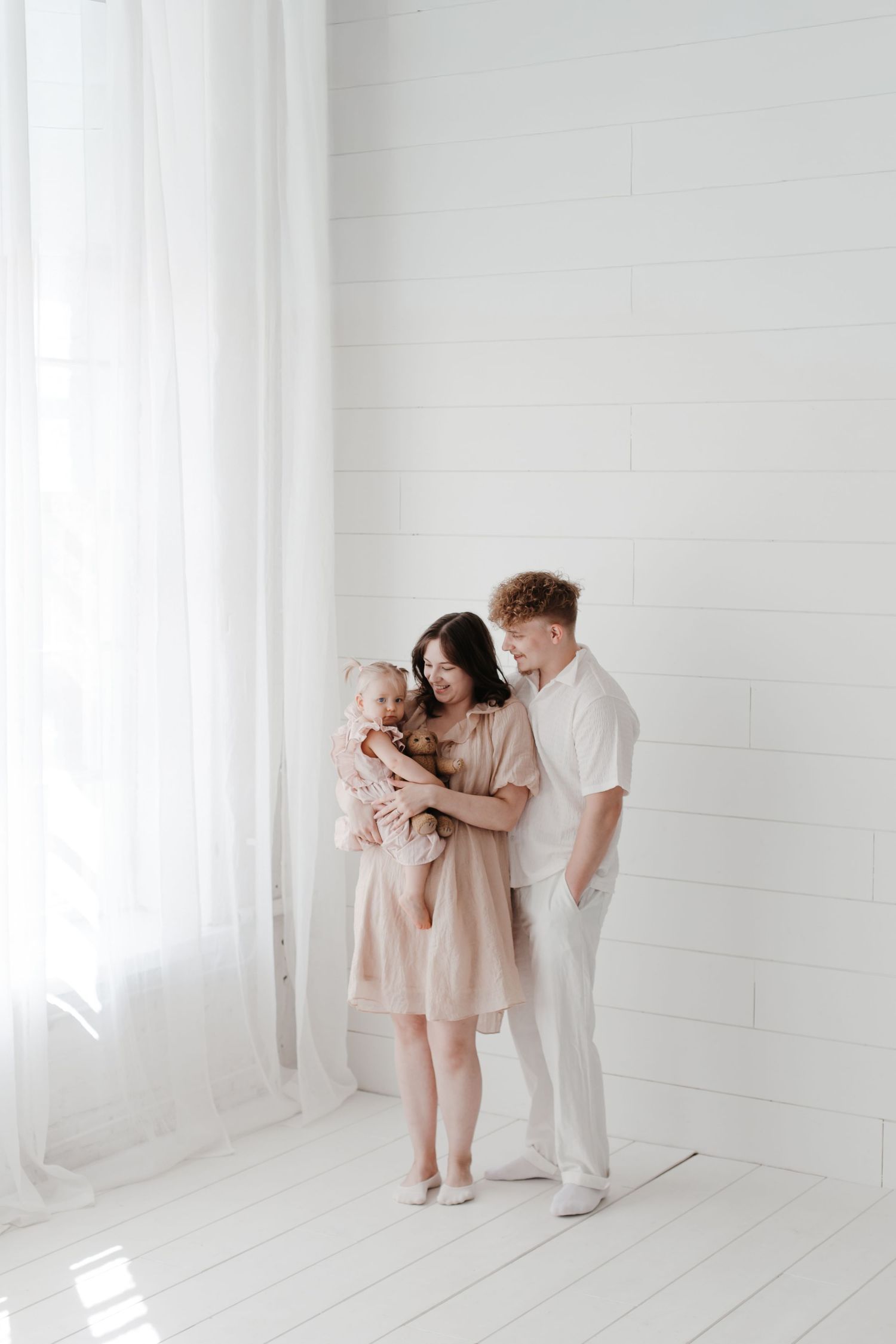 Family portrait in neutral tones against white shiplap wall and flowing curtains.
