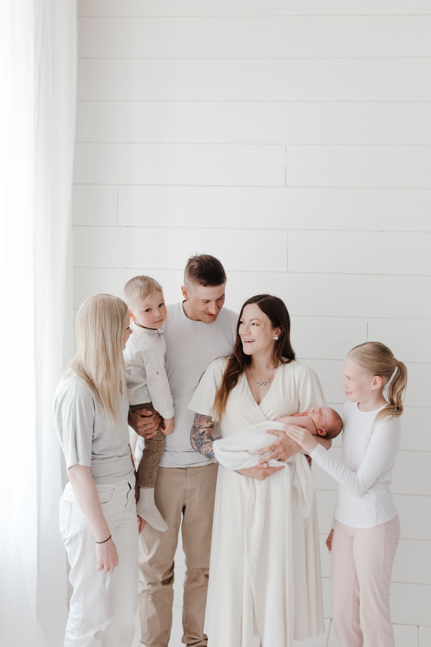 Family members sharing loving moments with newborn in bright white studio setting.