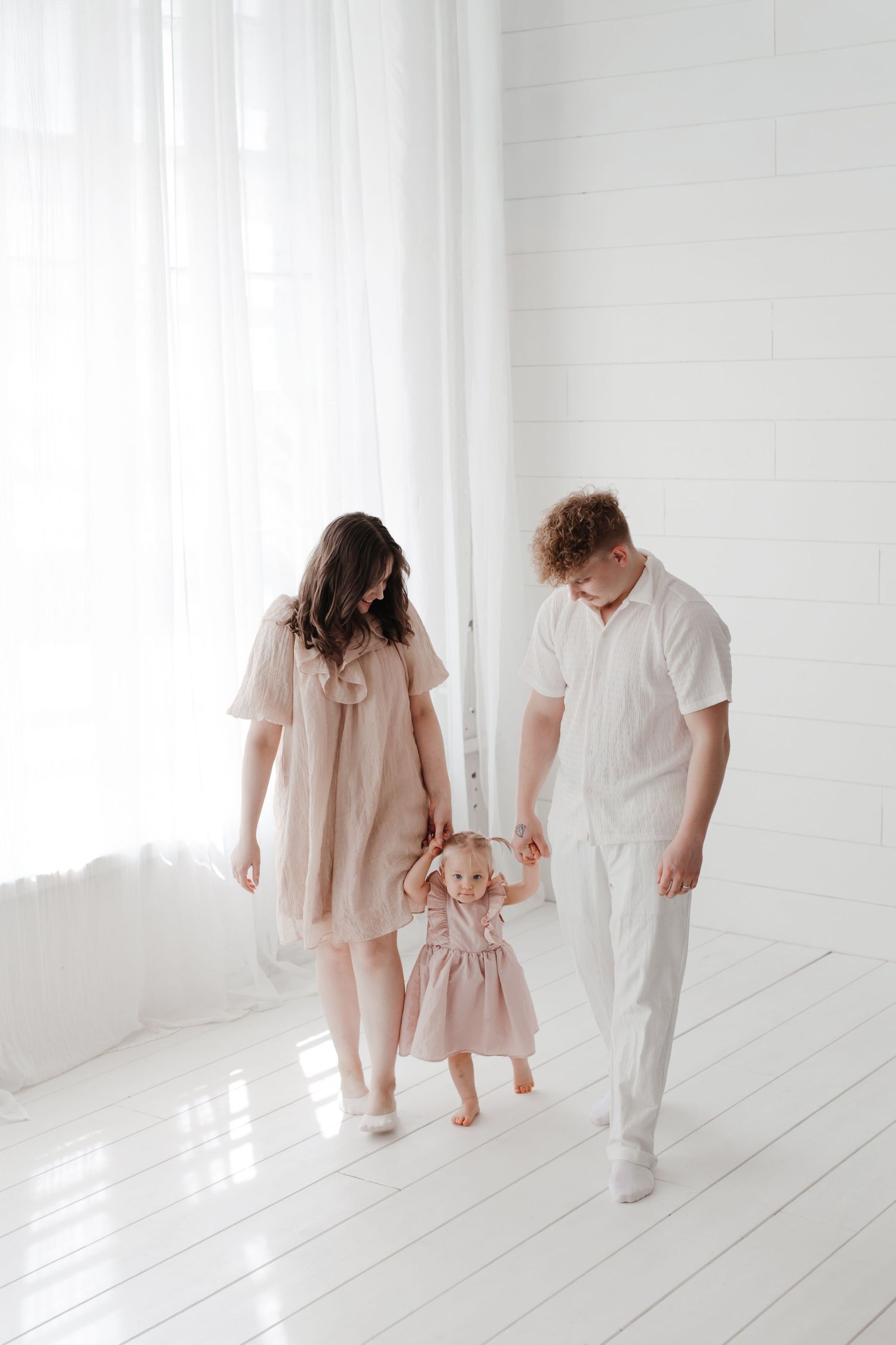 Family members walk together in coordinated white and pink outfits in a bright studio setting.