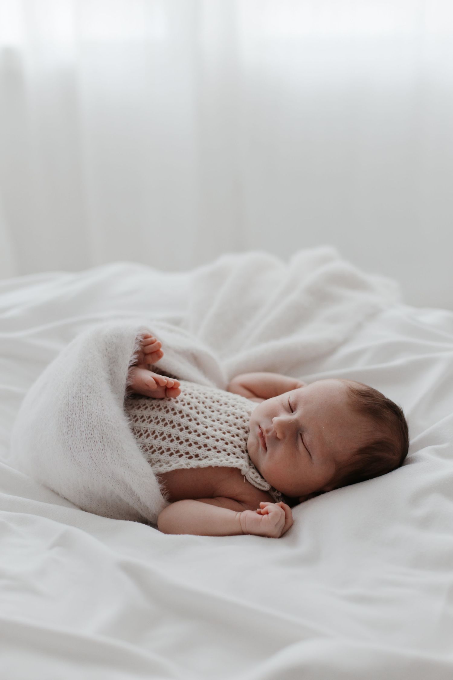 Sleeping infant in knitted outfit wrapped in cozy white blanket.