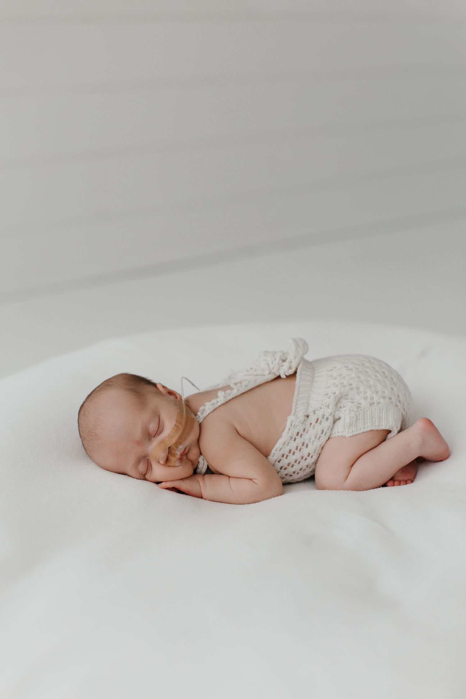 Peaceful newborn baby sleeping on white blanket wearing knitted cream-colored outfit.