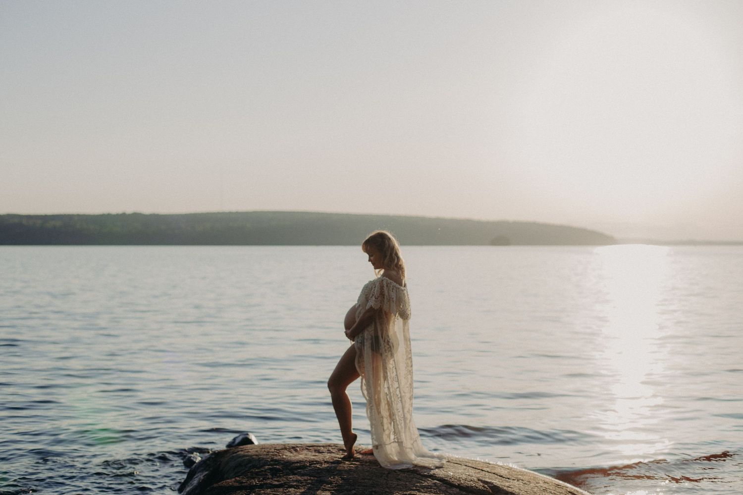 Silhouetted figure stands at the edge of a serene lake during sunset, creating a peaceful waterfront scene.