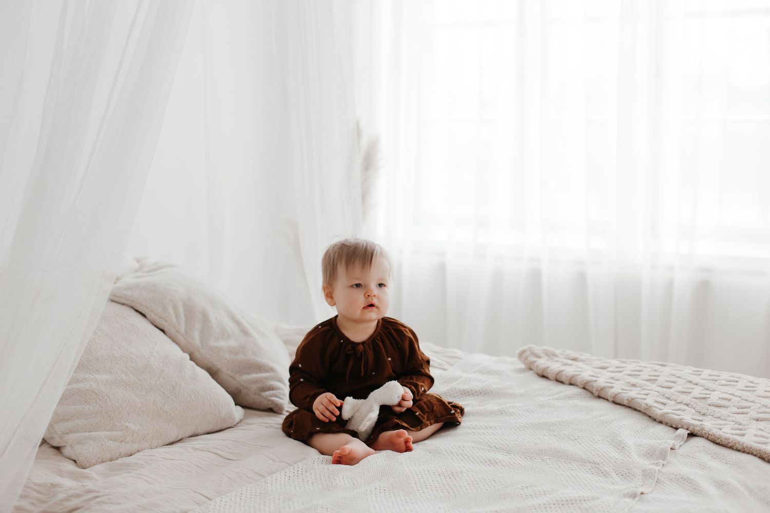 A bright white bedroom with natural light streaming through sheer curtains.