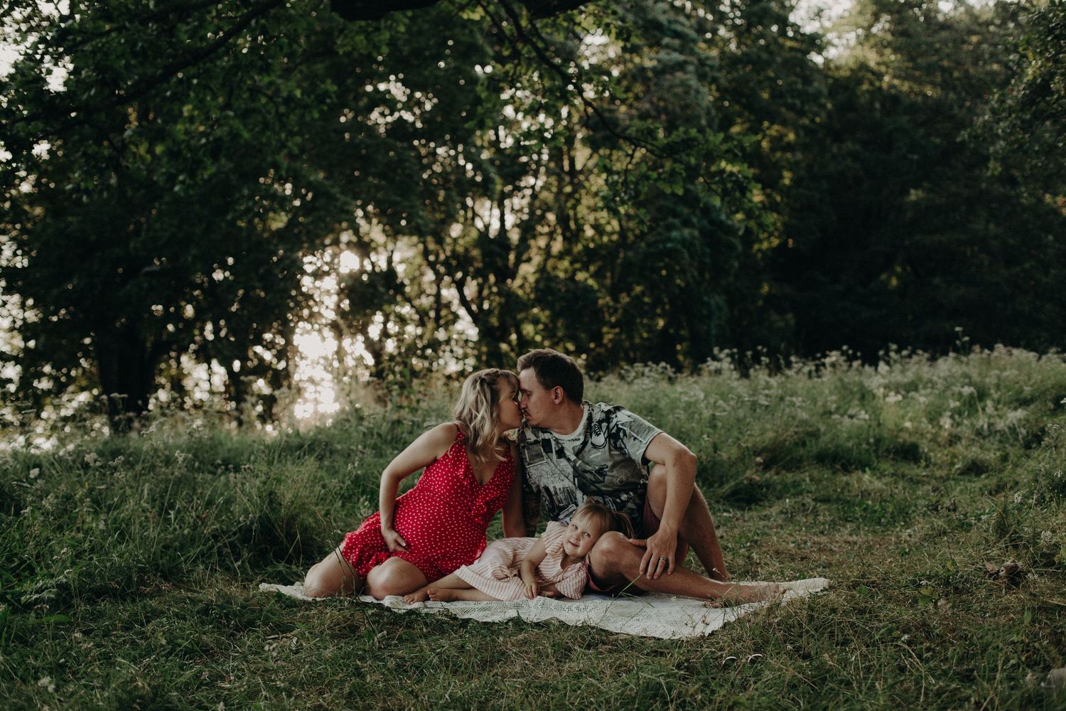 Natural light photography session with subjects resting on white blanket in park setting.