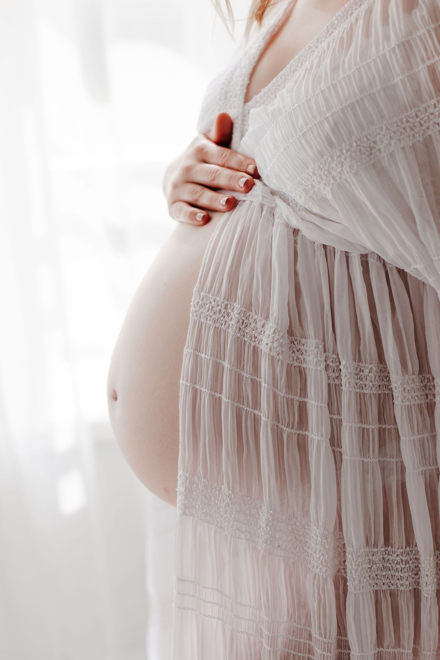 Elegant white tiered lace maternity dress photographed in soft window light.