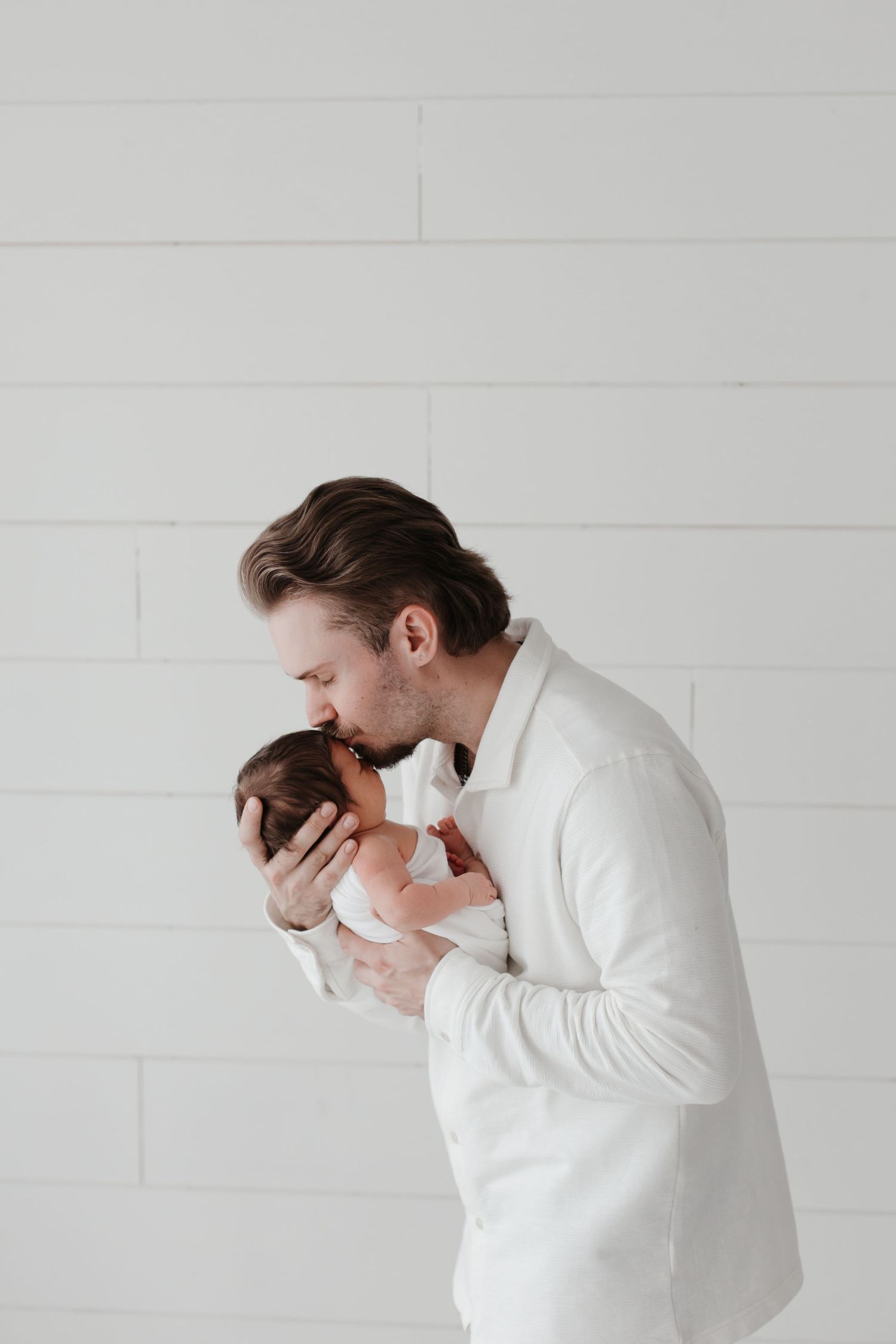 Parent in white shirt showing emotional reaction while holding baby.