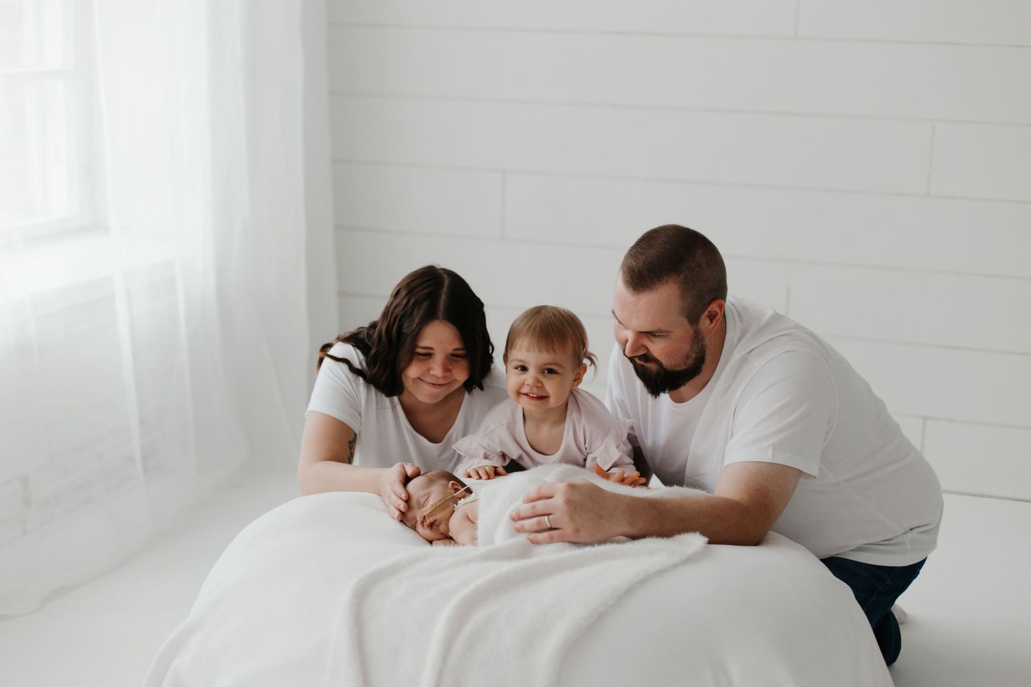 Family lying together on white bedding during an intimate photo session.