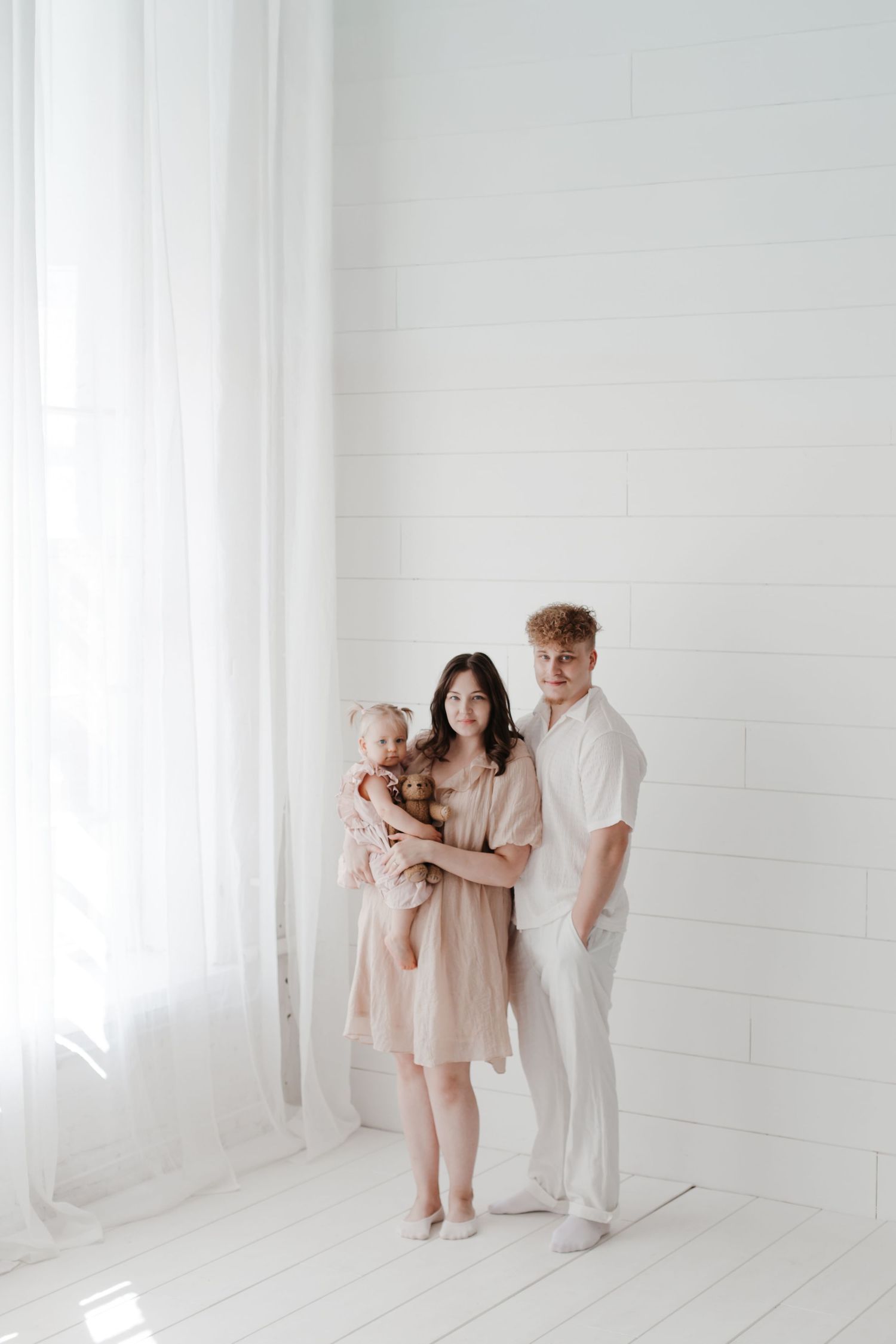 Modern family portrait in minimalist white room with natural window light.