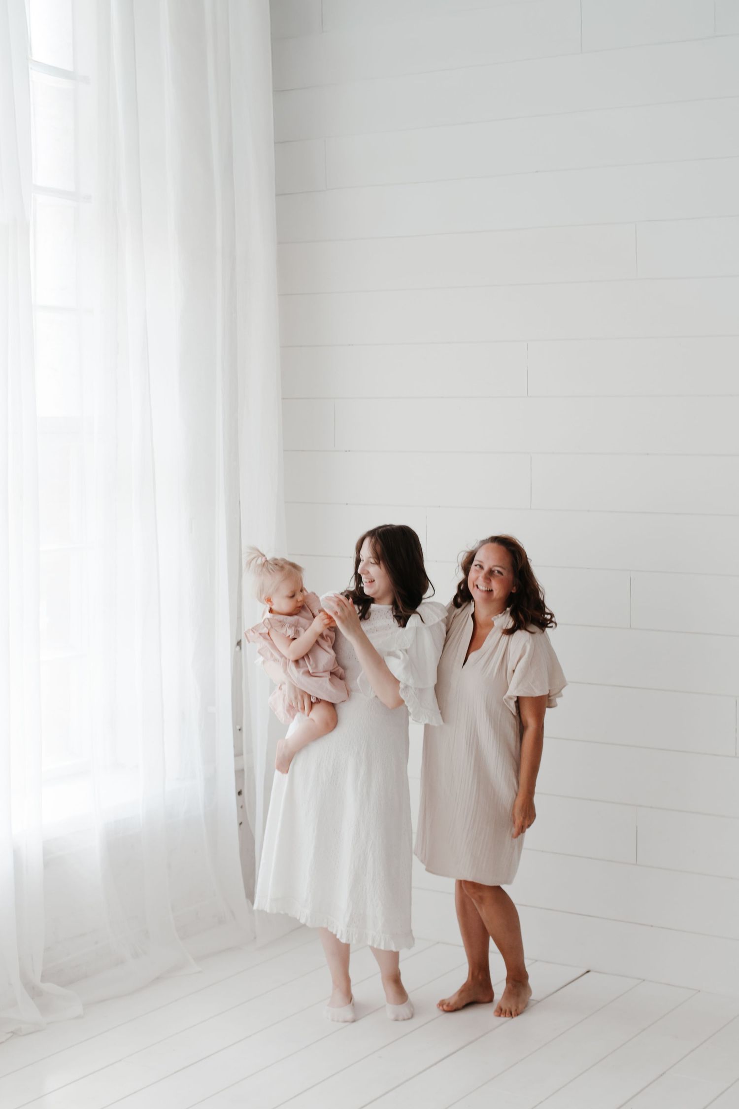 Group in white outfits interacts playfully in bright white studio space.