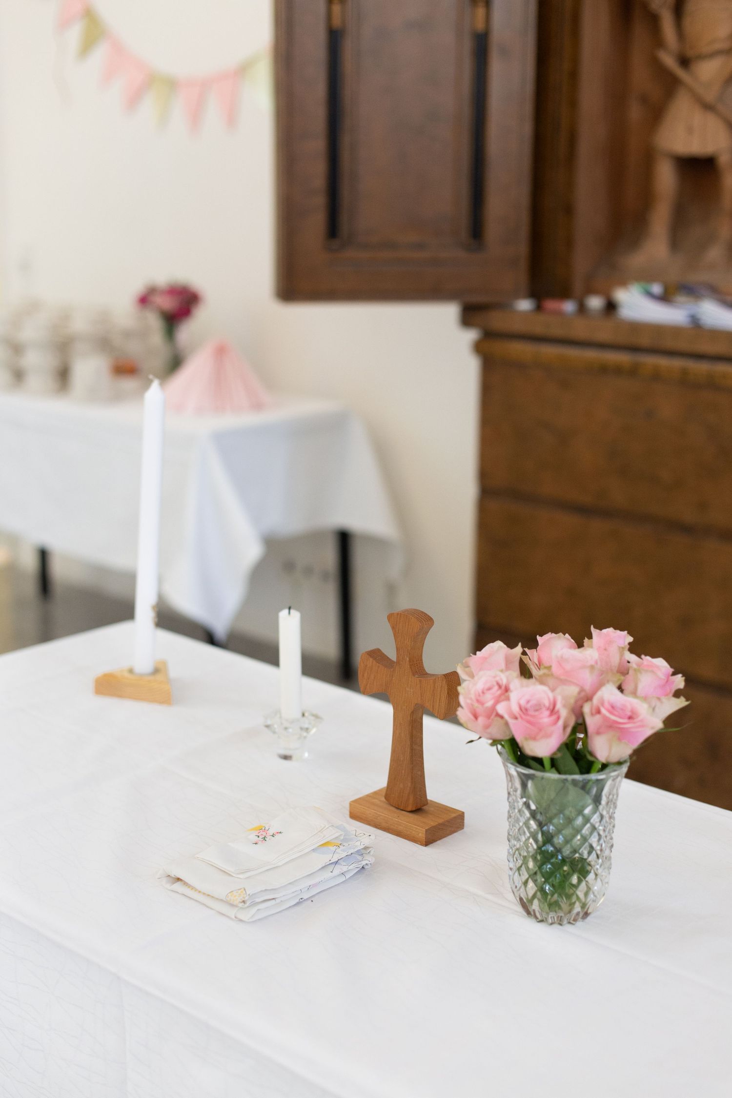 White table decorated with pink roses, candles and wooden cross for baptism or communion.