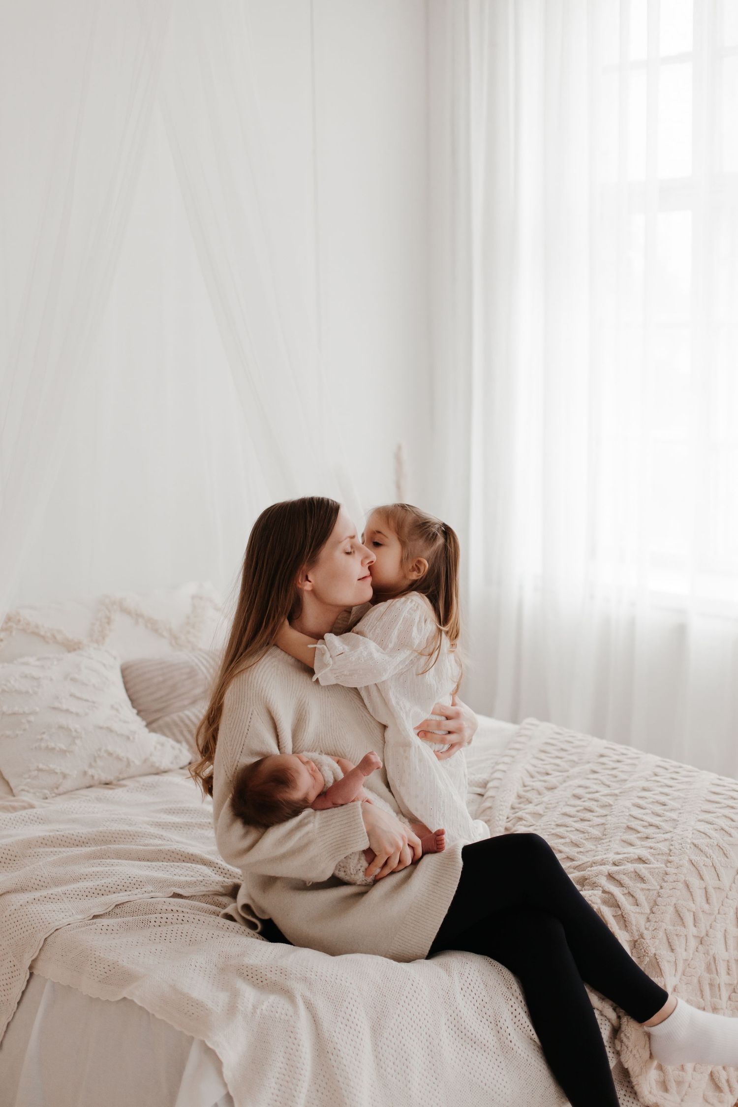 Family sharing intimate moments together on white bedding in soft natural light.
