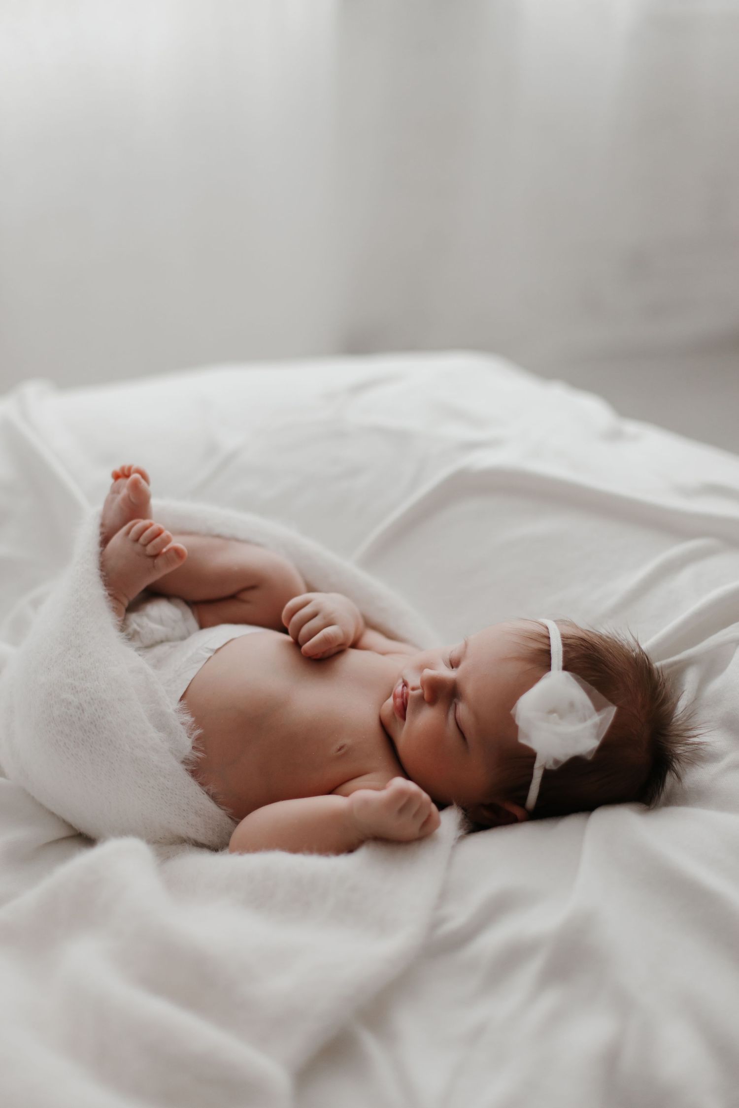 Newborn baby wrapped in soft white bedding lying peacefully on bed.