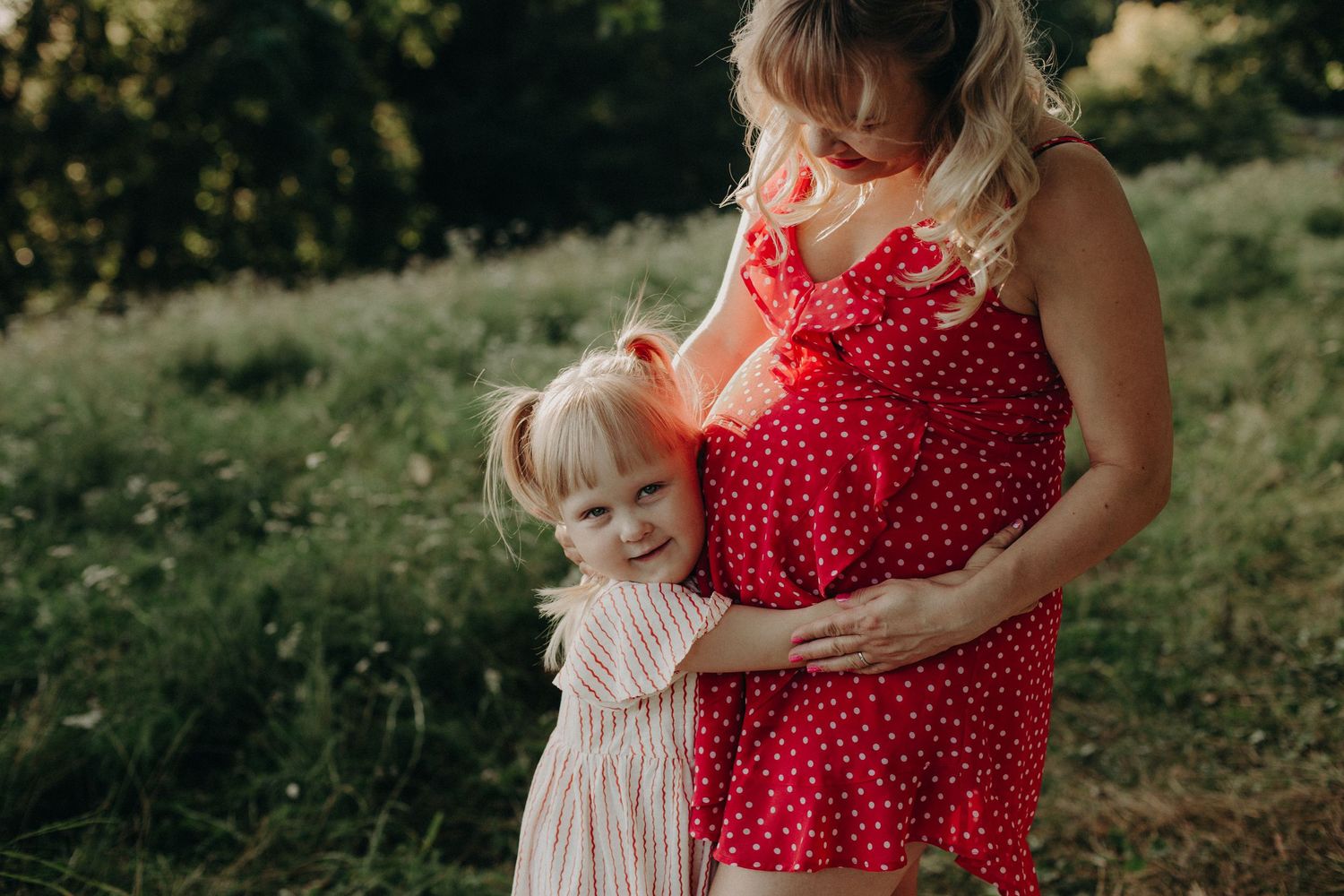 Outdoor maternity session featuring red polka dot dress in natural setting.
