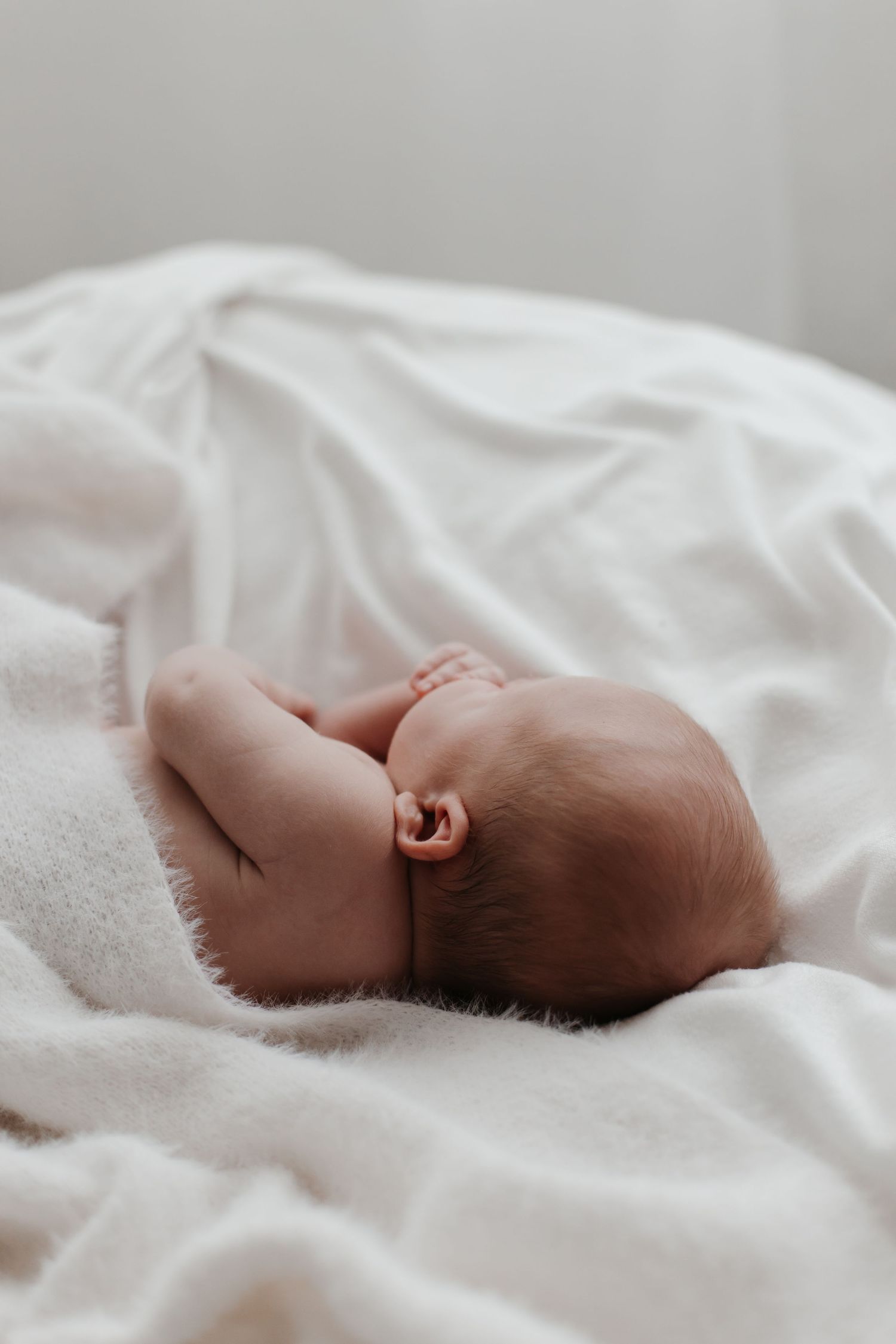 Baby resting peacefully on white sheets in minimalist setting.