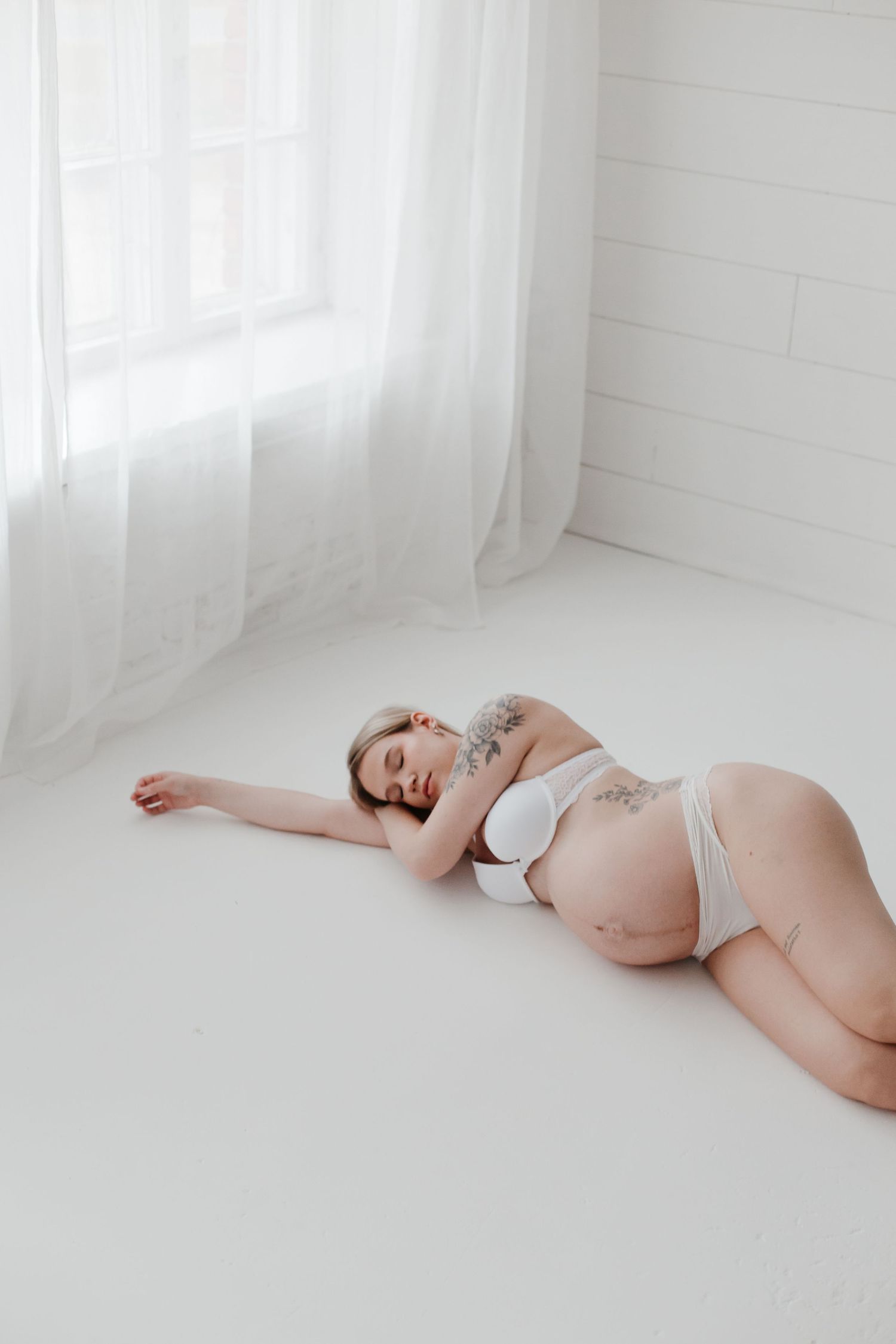 Peaceful maternity portrait on white floor with soft natural lighting.