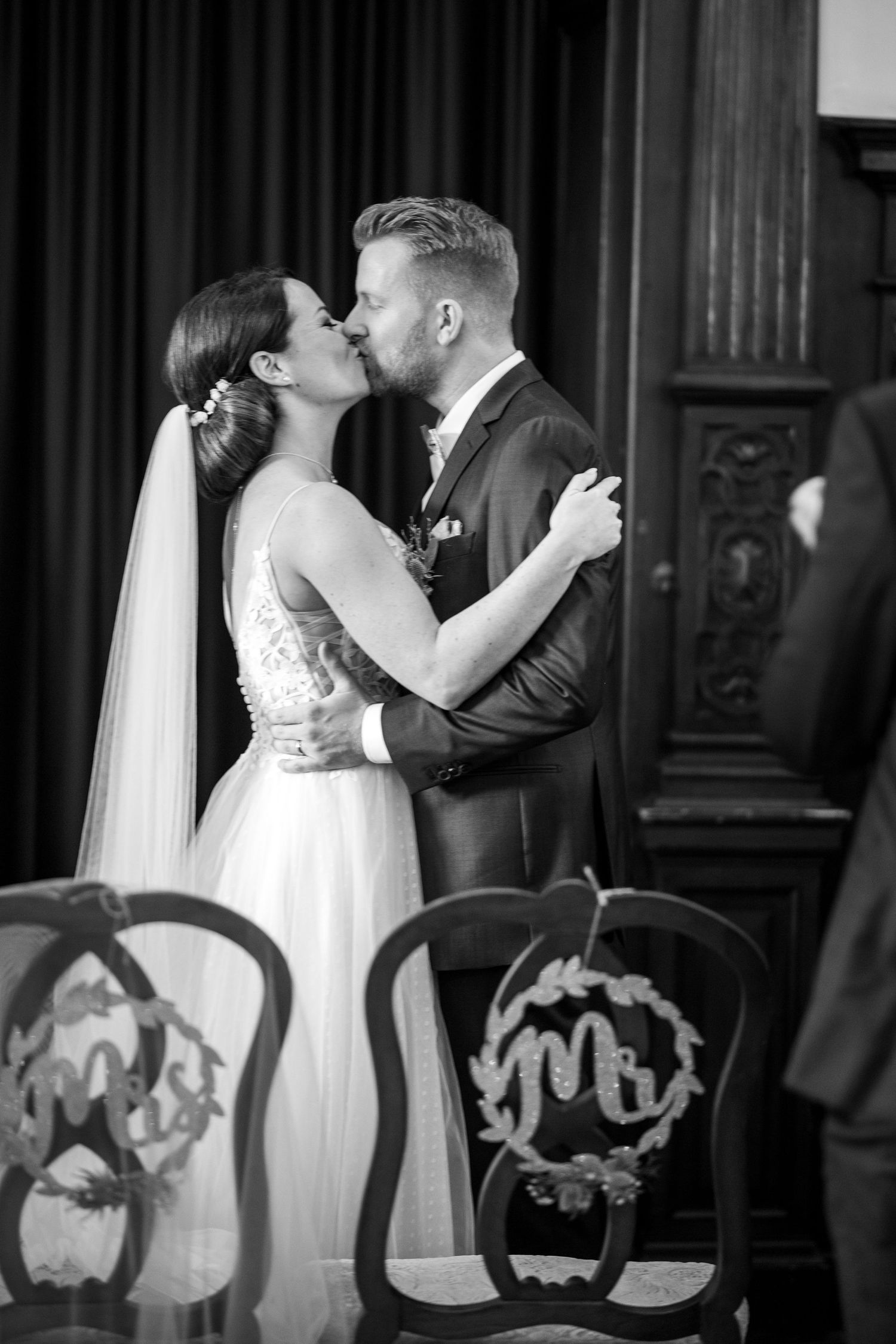 Black and white photo of a bride and groom sharing their first kiss at the altar during their wedding ceremony.