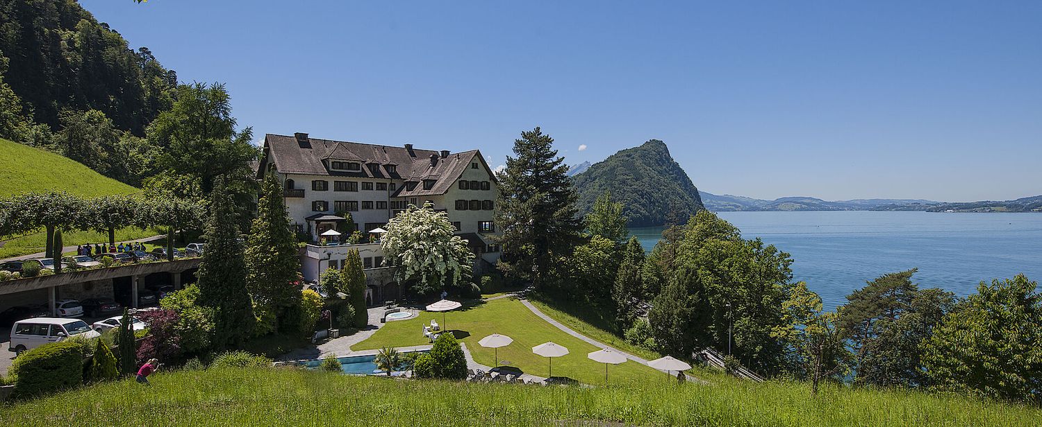 Luxury mountain resort hotel overlooking a scenic lake with manicured grounds and pool.