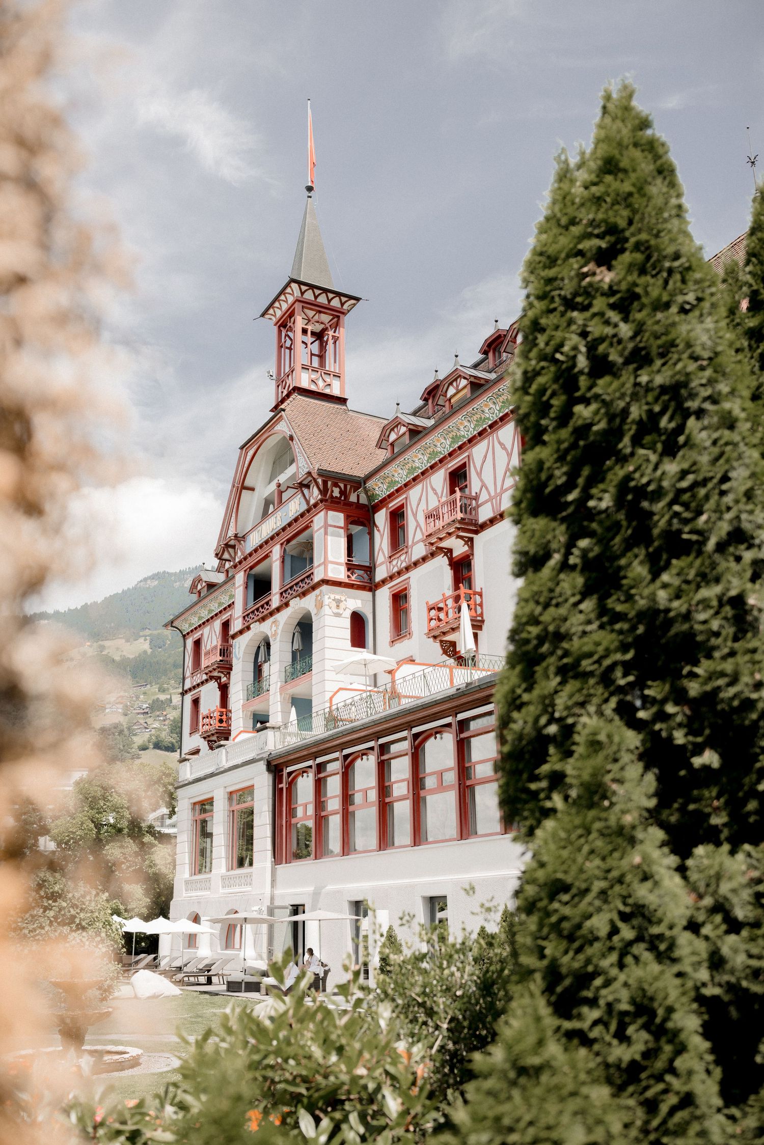 A grand historic hotel with red and white architecture nestled among trees in a mountainous setting.