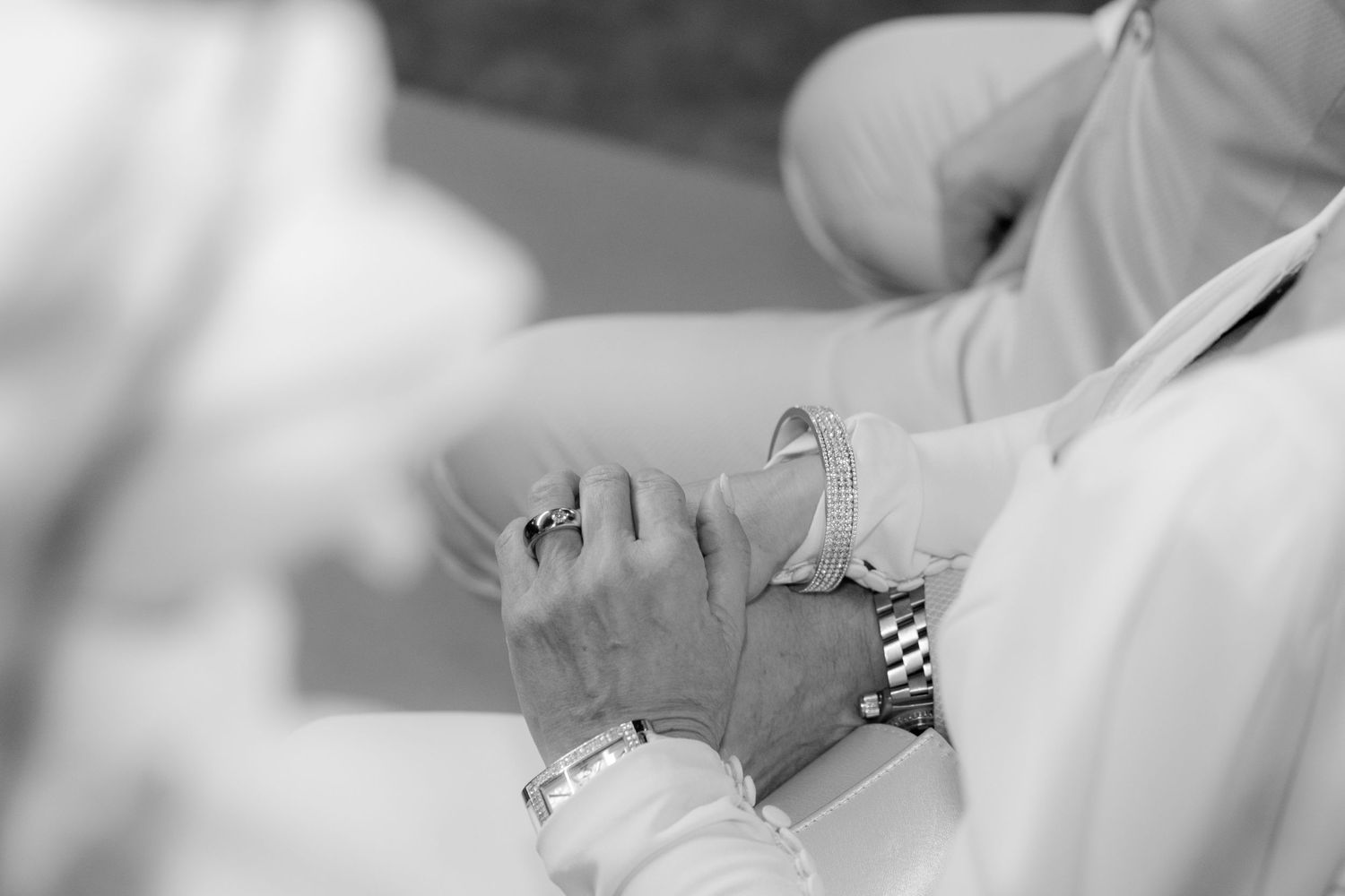 Black and white photo of couple holding hands, showing rings, bracelet, and watch at a wedding ceremony.