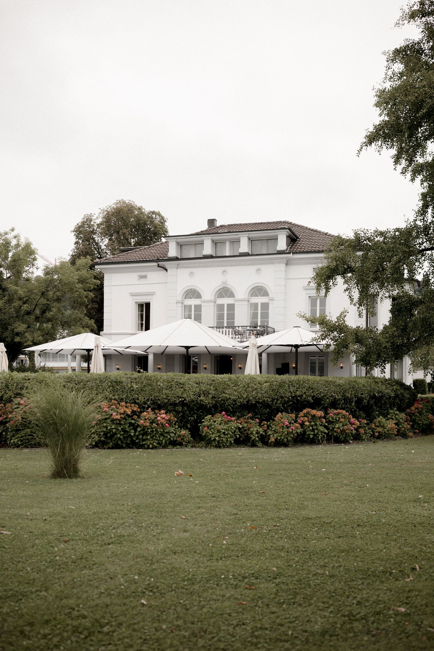 A white villa with arched windows and outdoor umbrellas surrounded by manicured gardens.
