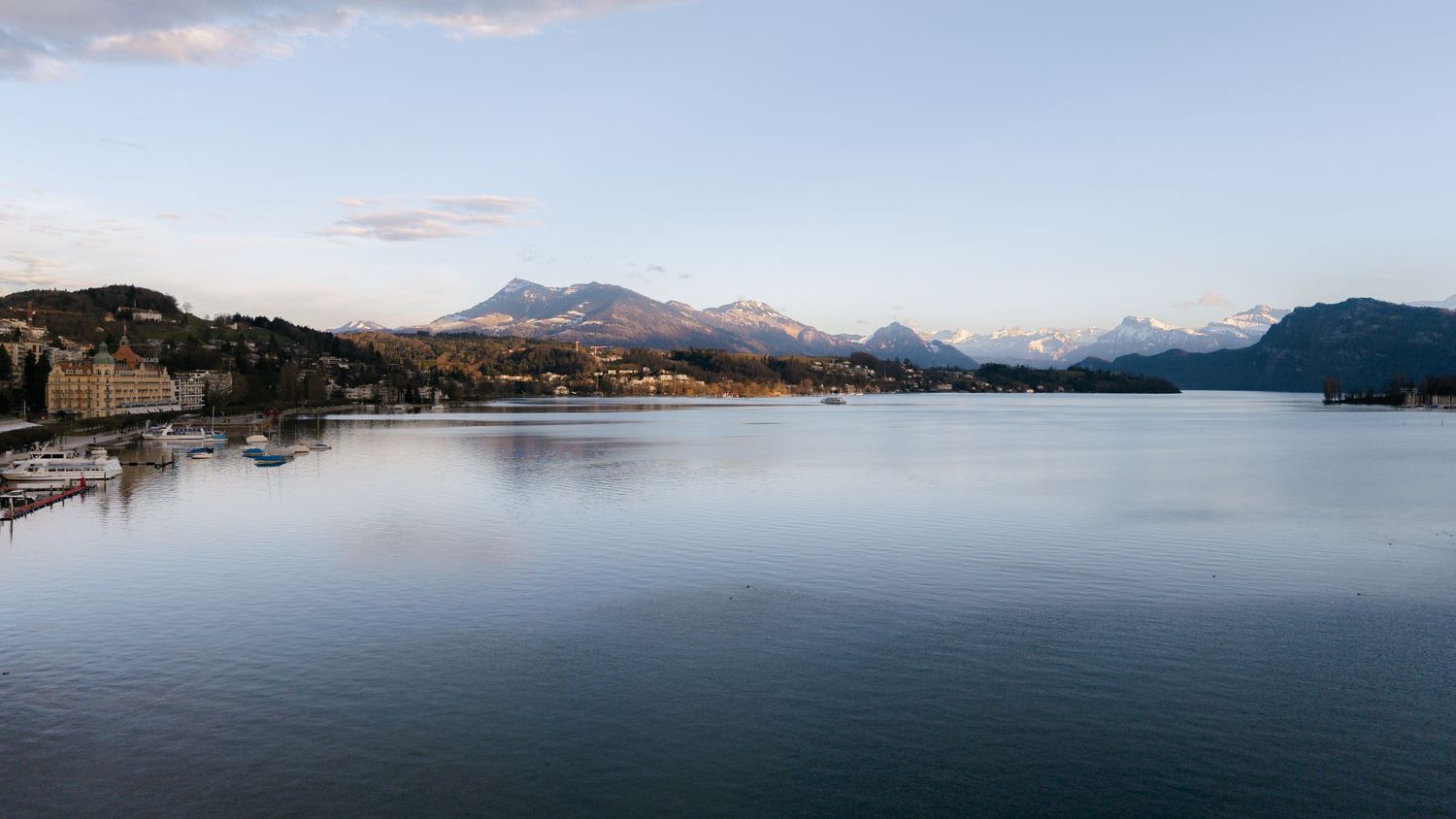 Calm panoramic view of Lake Lucerne with snow-capped Swiss Alps and waterfront town at dusk.