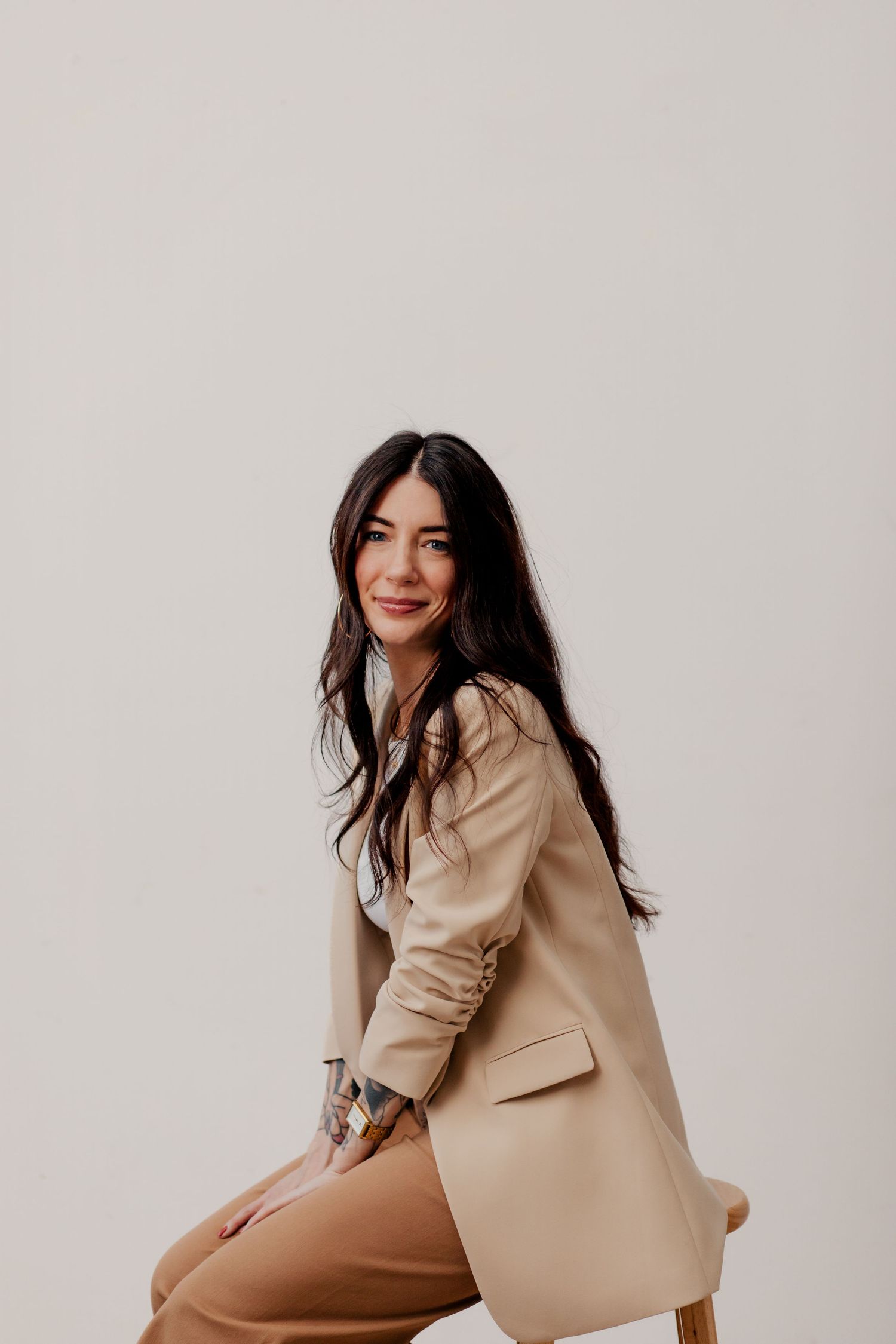 Model in beige blazer and nude bodysuit poses in four creative positions against white background.