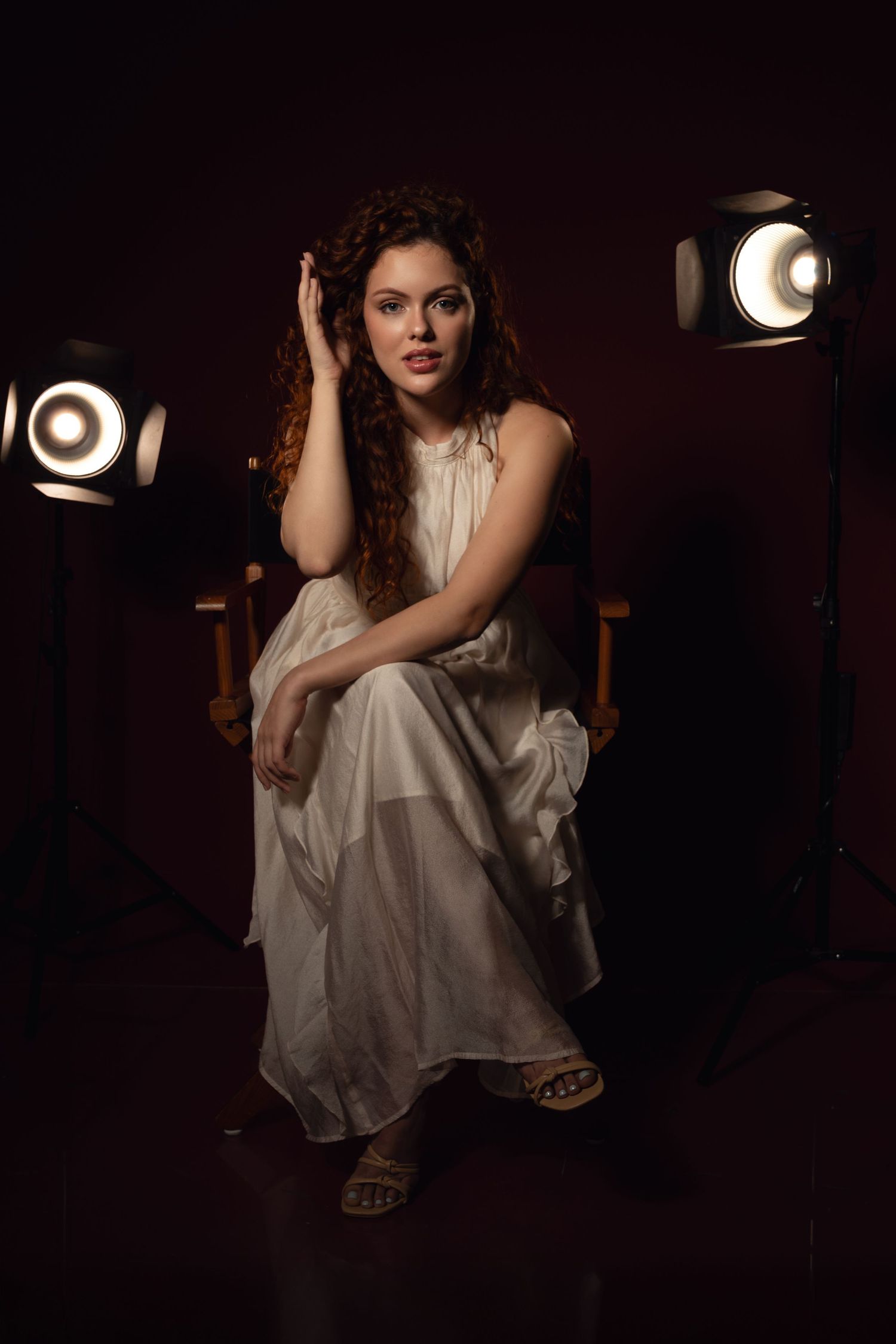 Dramatic studio portrait in white flowing outfit with moody lighting and dark background.