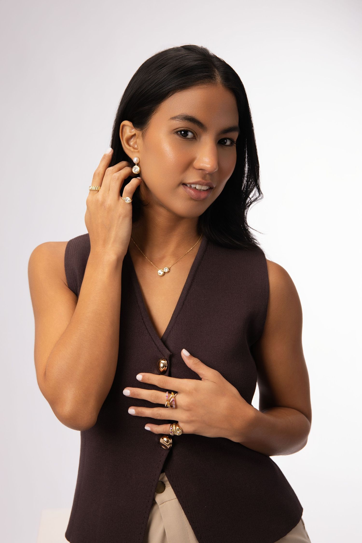 Professional portrait of woman in brown vest wearing delicate jewelry against white background.