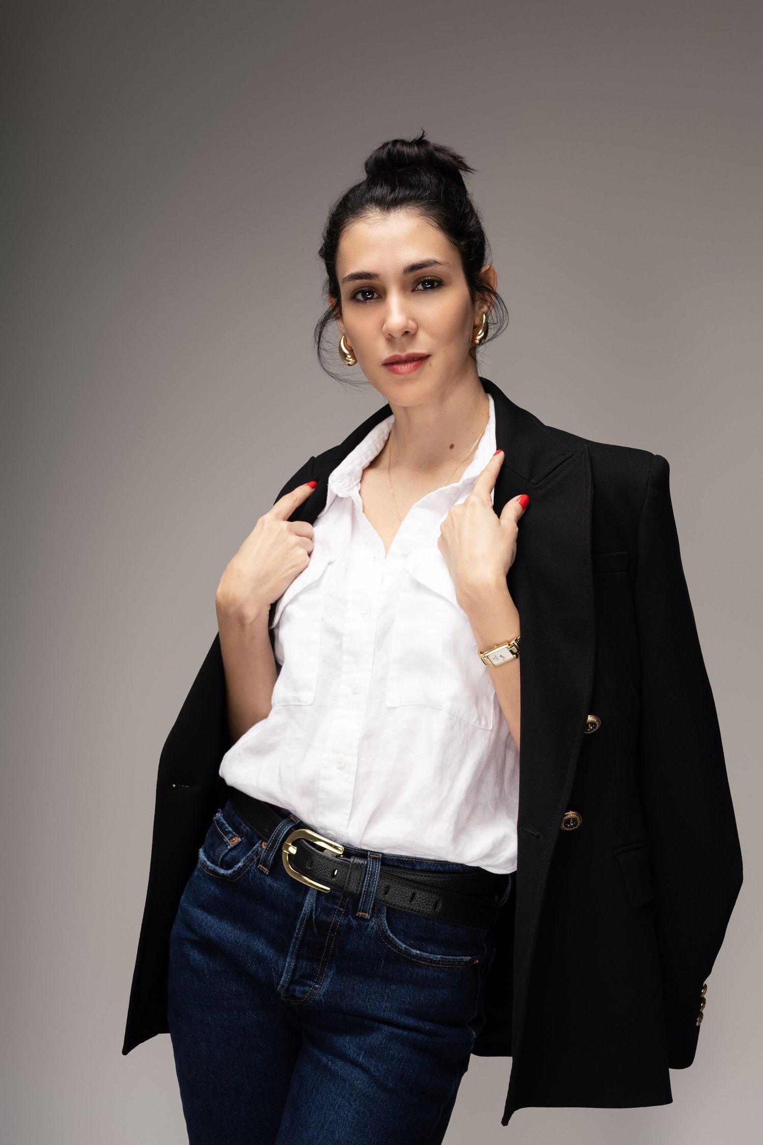 Modern business casual look with white shirt, black blazer and jeans against grey background.