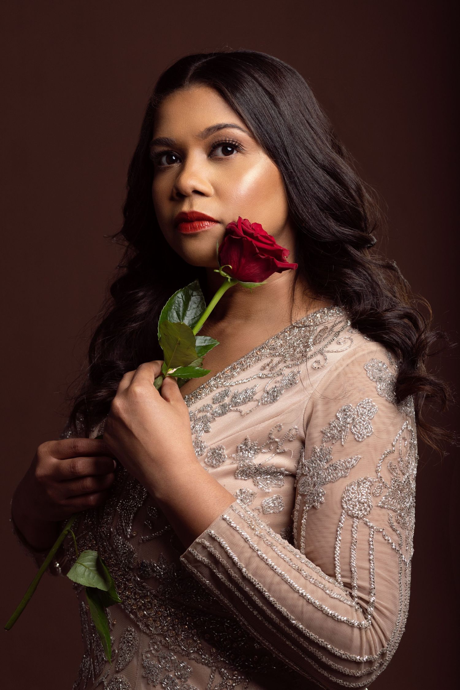 Glamour portrait with red rose against dark background in beaded dress.