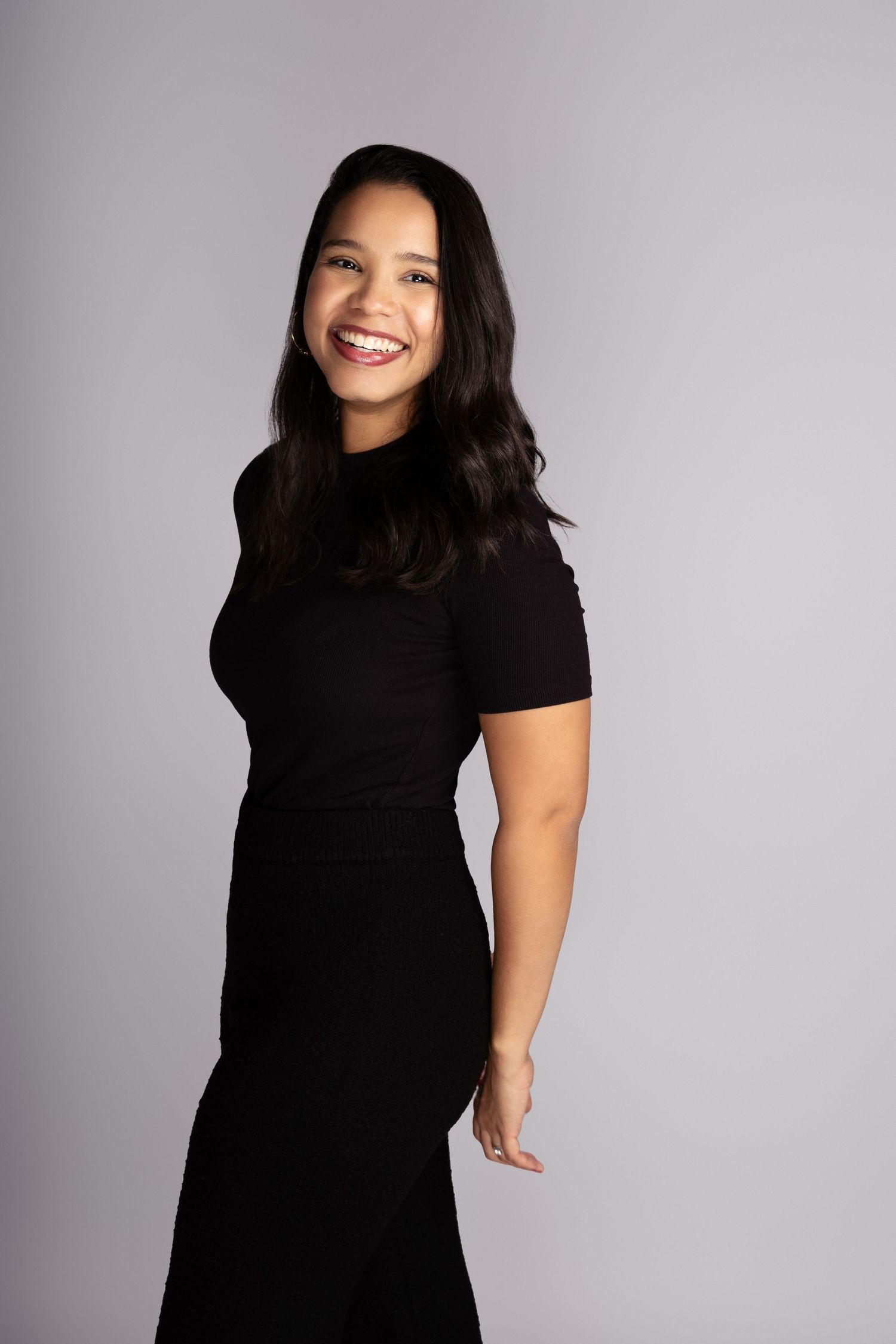 Woman in fitted black dress smiling against grey studio background.