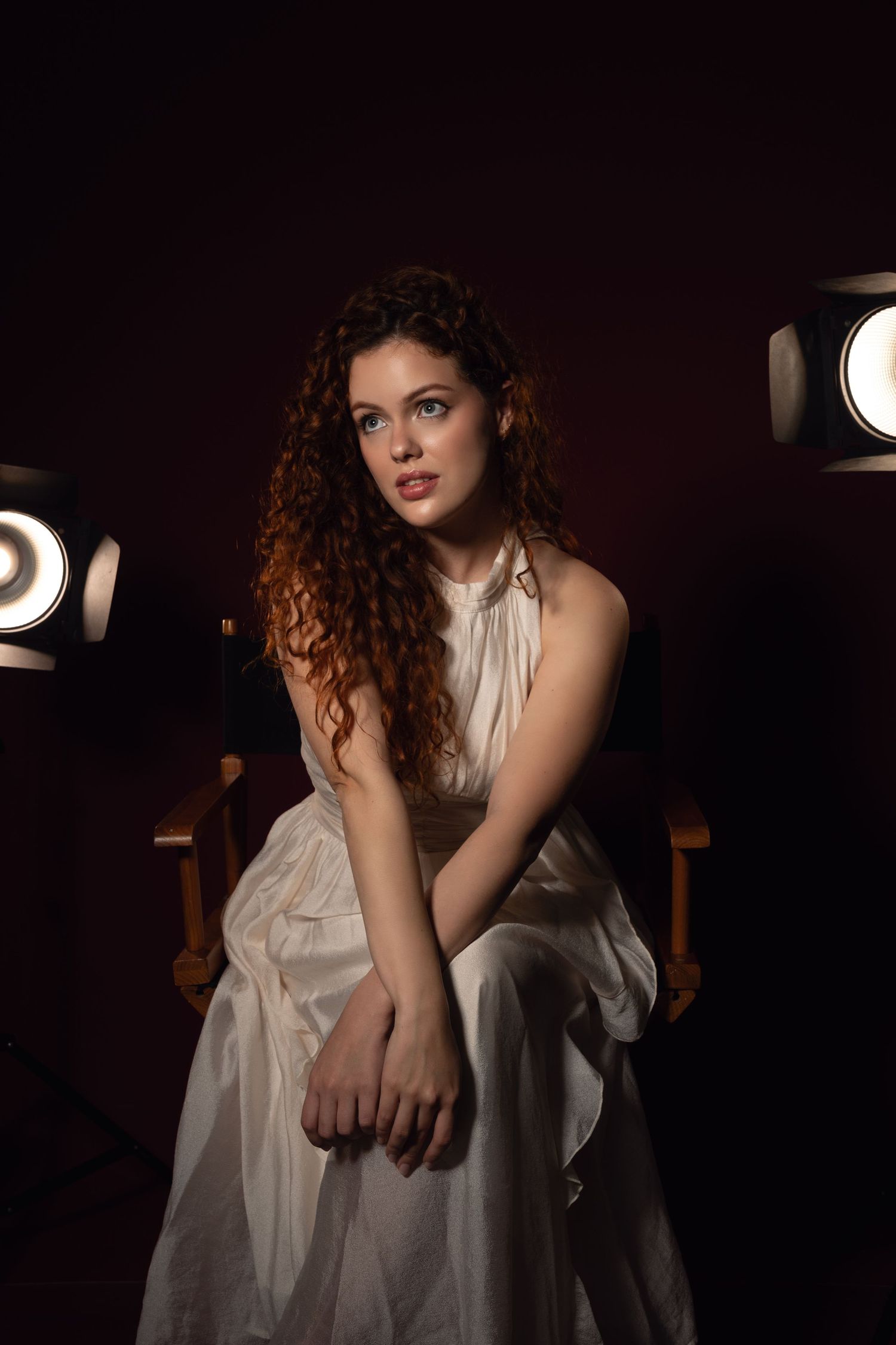 Dramatic low-key portrait in white dress against dark background with moody lighting.