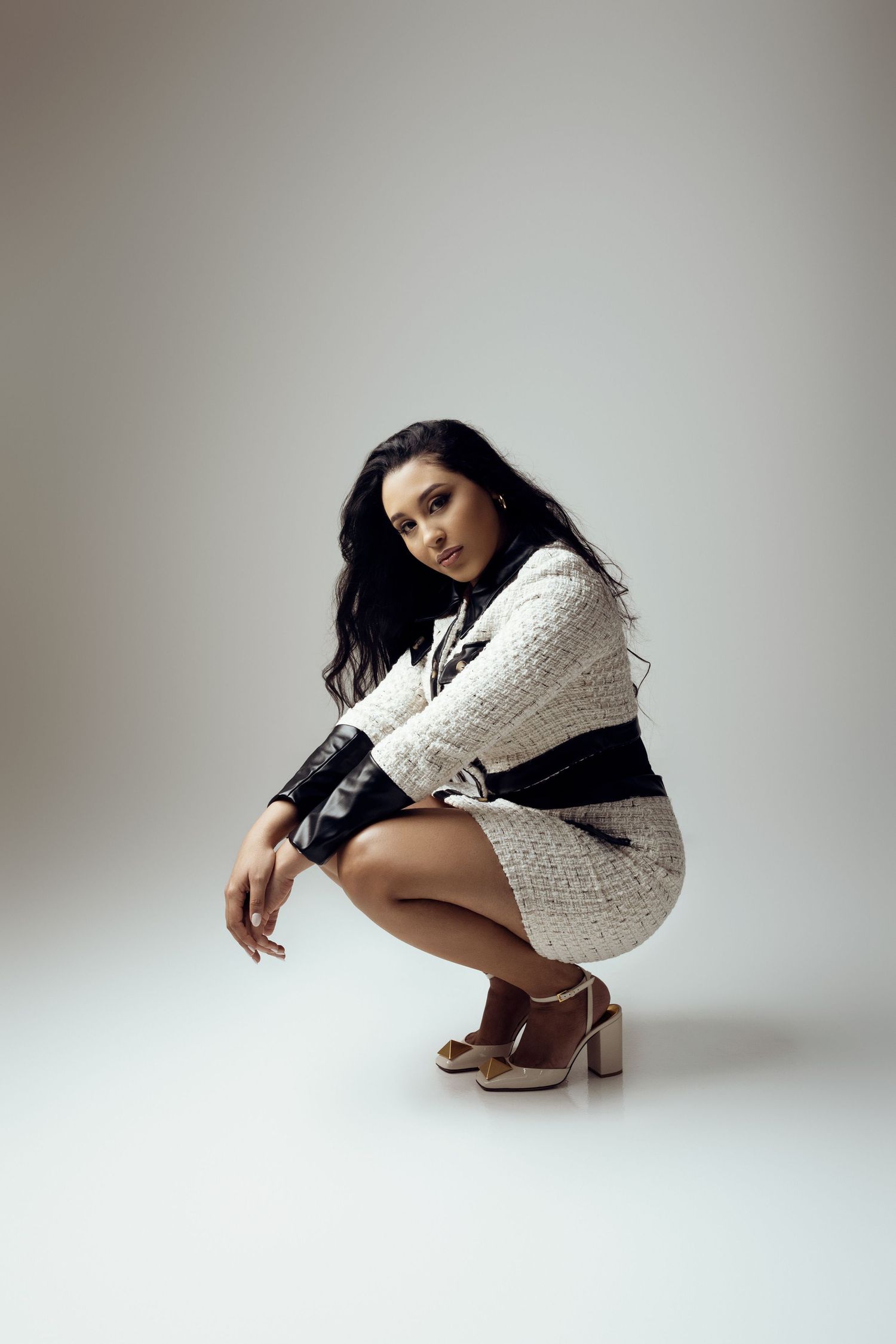 Model wearing black and white tweed ensemble crouches elegantly on studio floor.