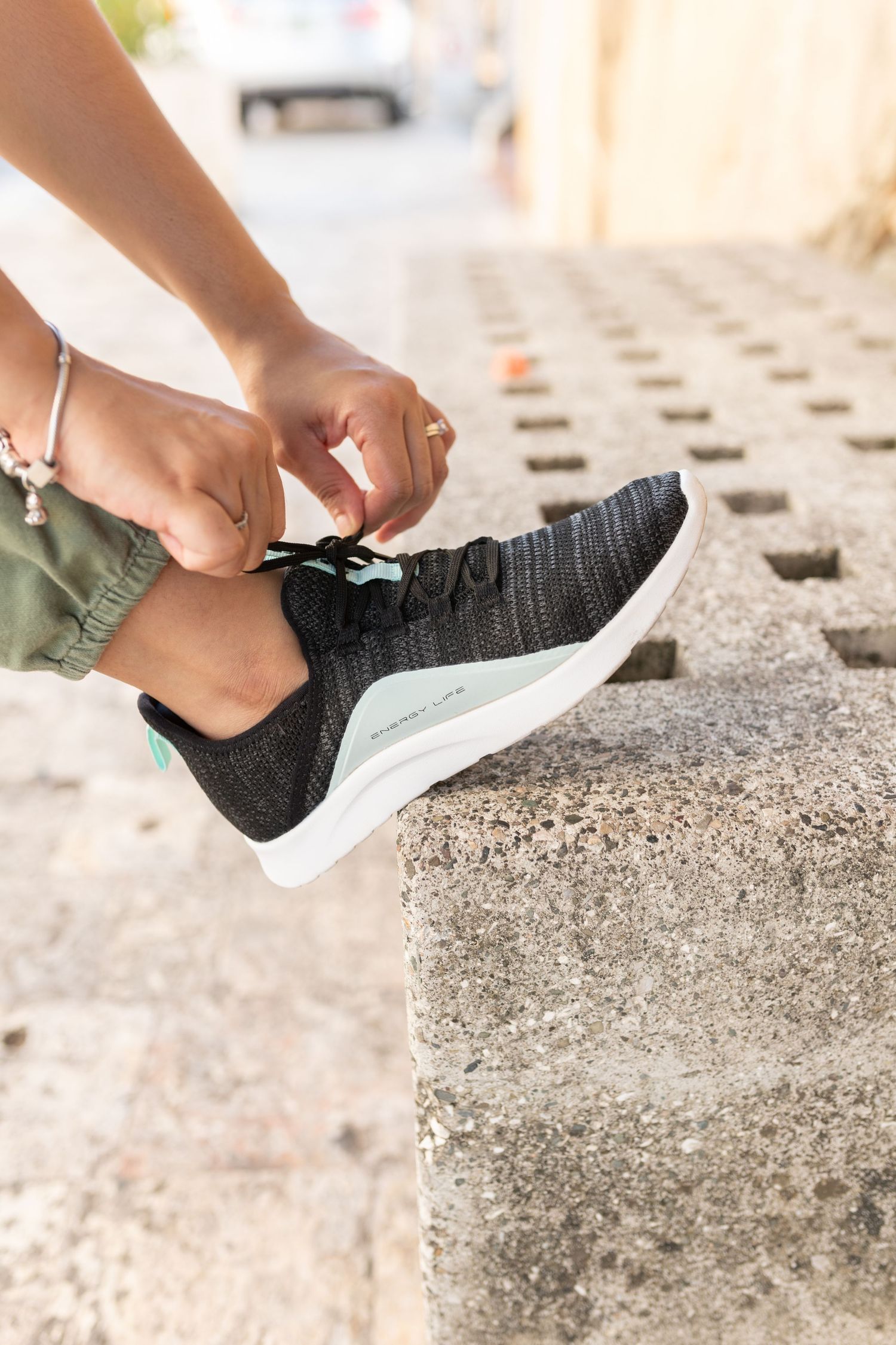 Person tying laces on black and mint green sneakers while sitting on concrete steps outdoors.